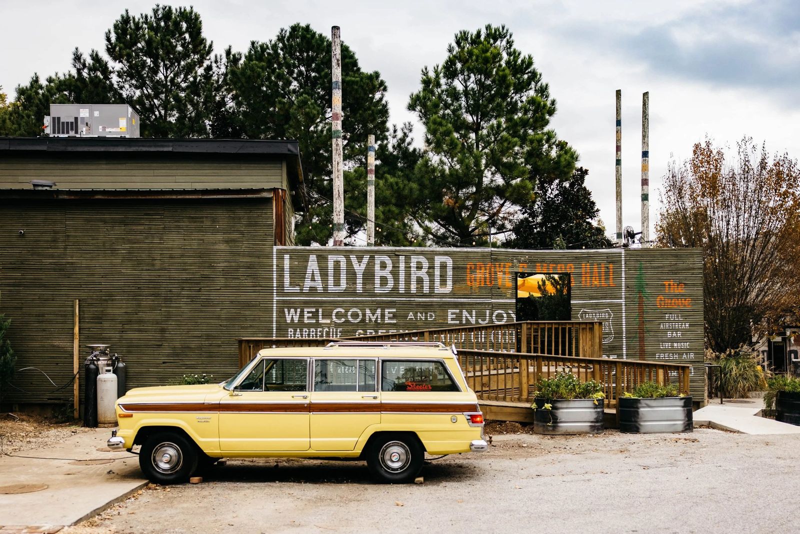 A yellow vintage SUV parked beside a weathered wooden fence with a Ladybird sign and smokestacks behind