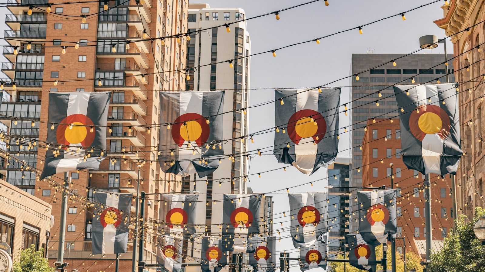 String lights and hanging banners over a street between tall brick buildings.