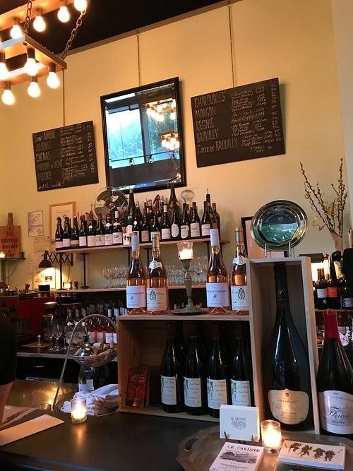A wine bar counter with shelves of wine bottles, chalkboard menus and a mirror on the wall, and candles in the foreground.