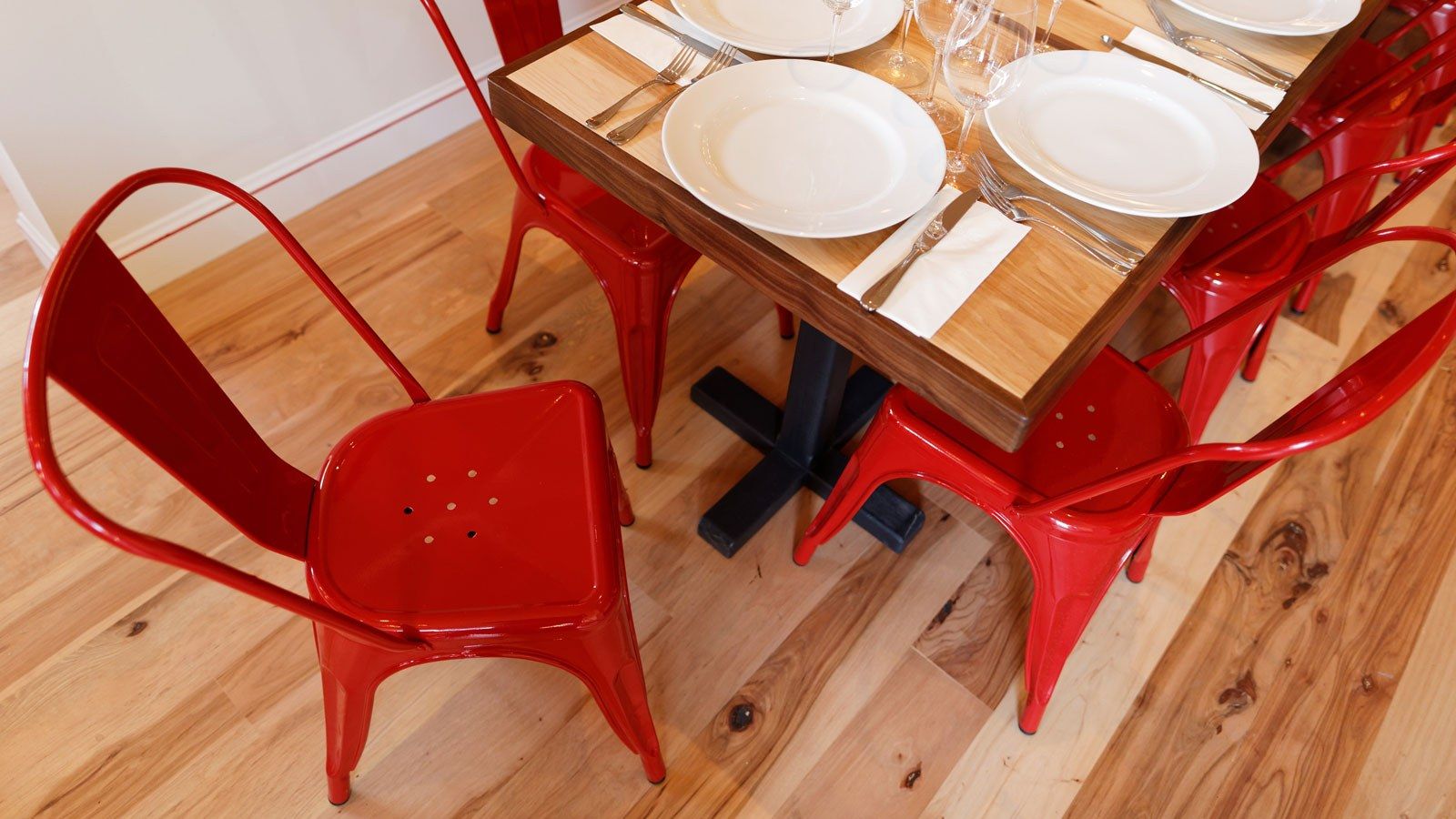 Wood table set with plates and glasses beside red metal chairs