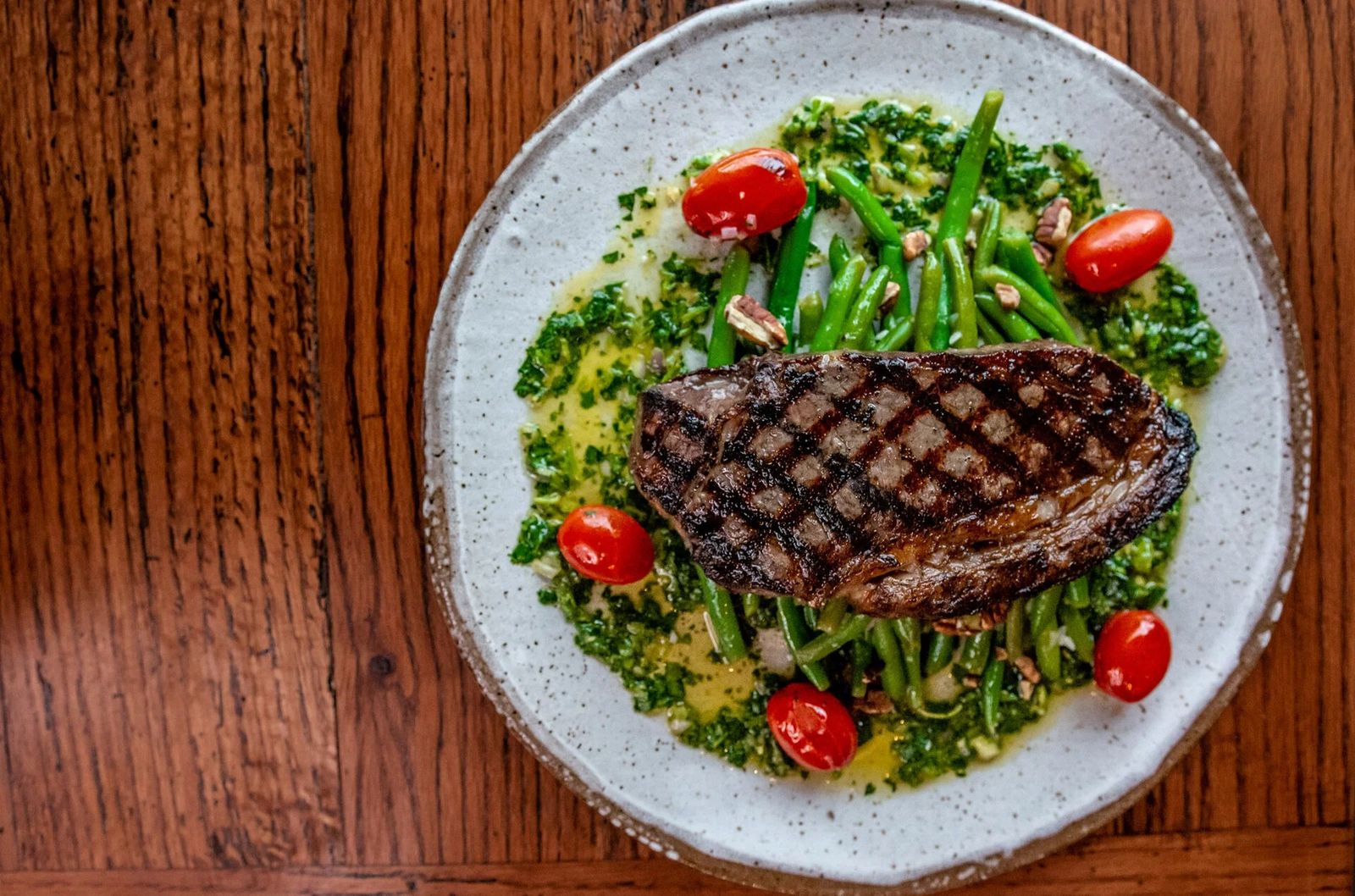 Grilled steak on a speckled plate with green beans and cherry tomatoes on a wooden table