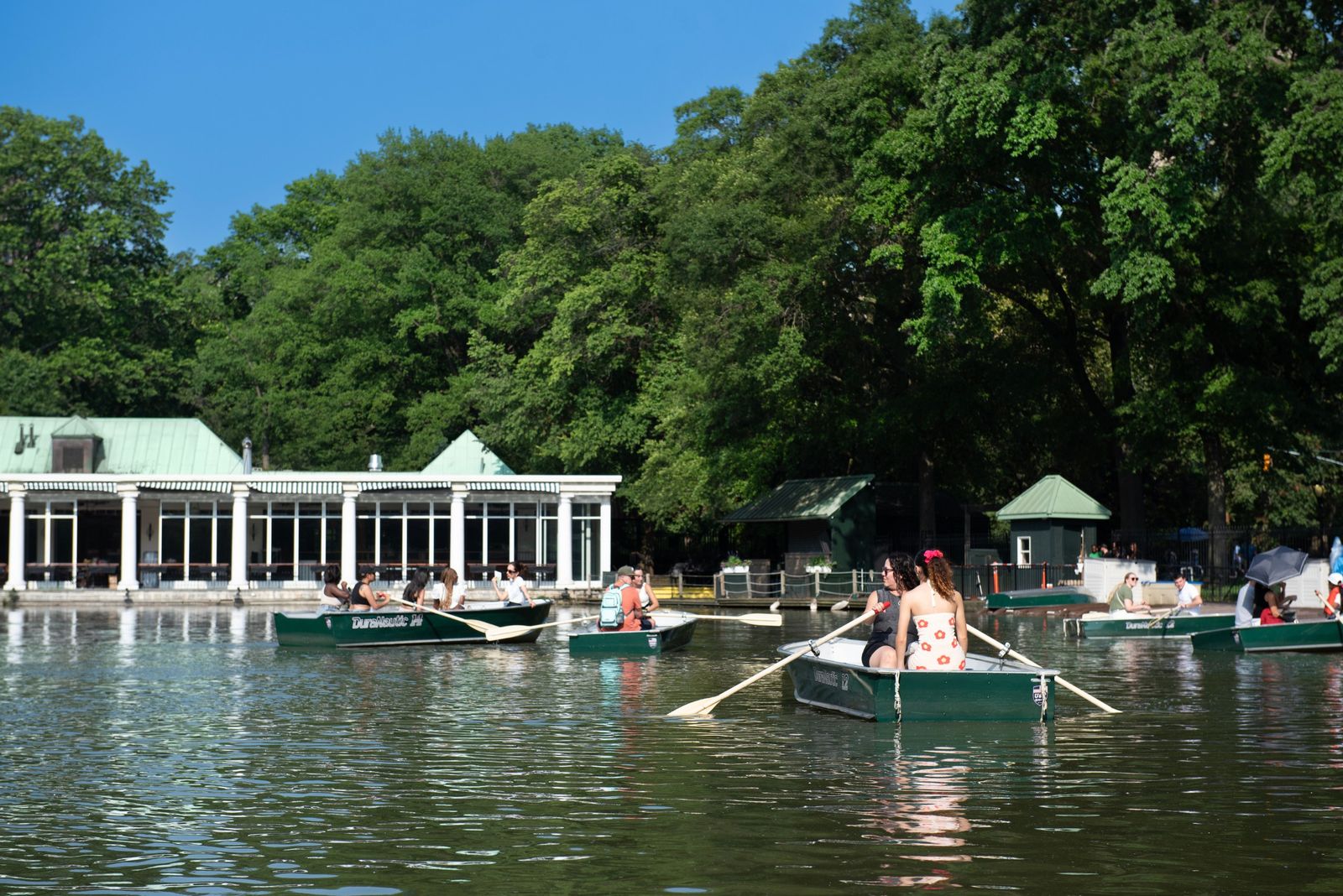 The Central Park boathouse on the lake with rowboats on the water and trees behind