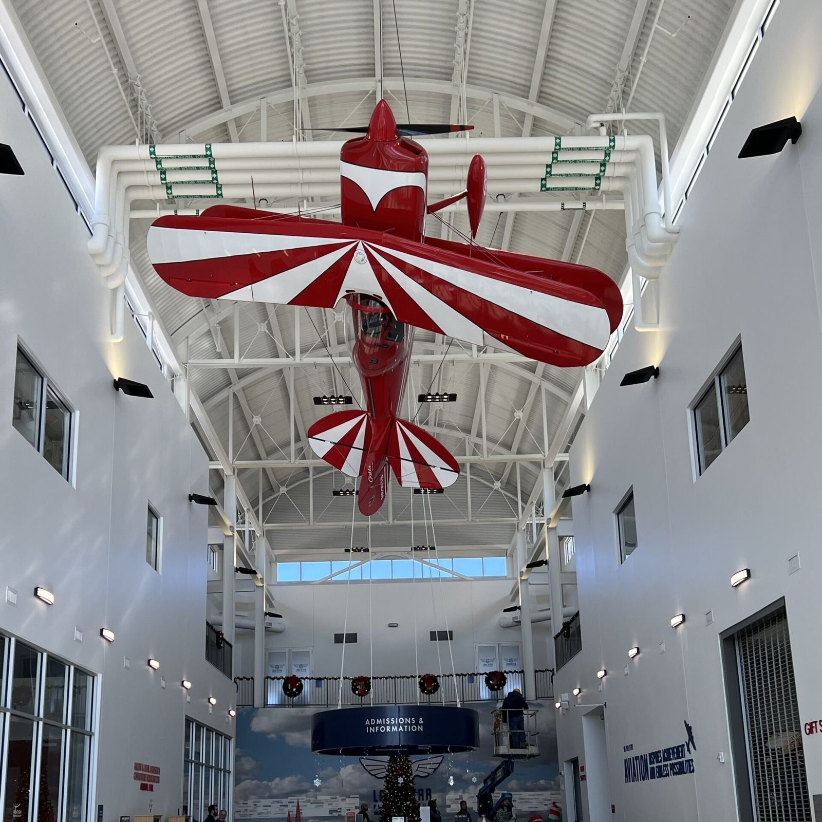 A red and white biplane suspended from the ceiling of a bright museum hall