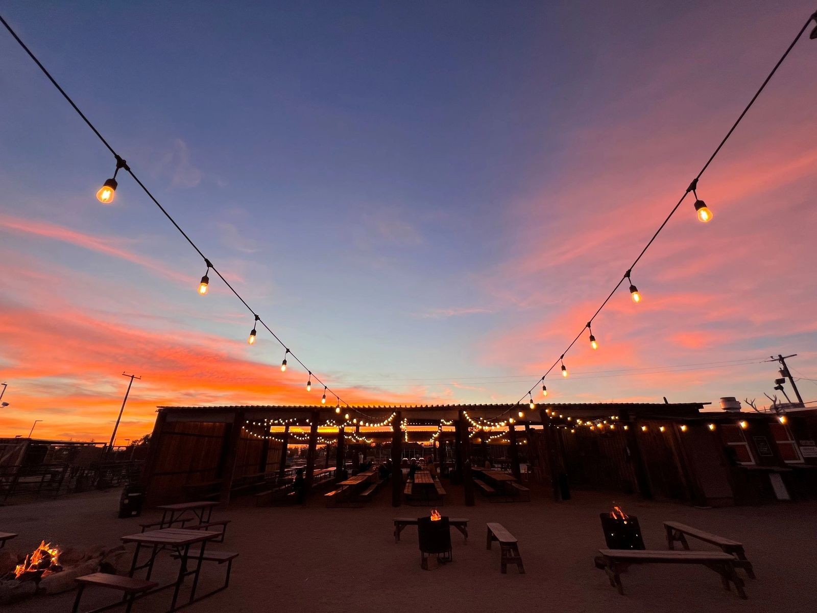 String lights over an adobe-style ranch courtyard against a pink and orange sunset sky