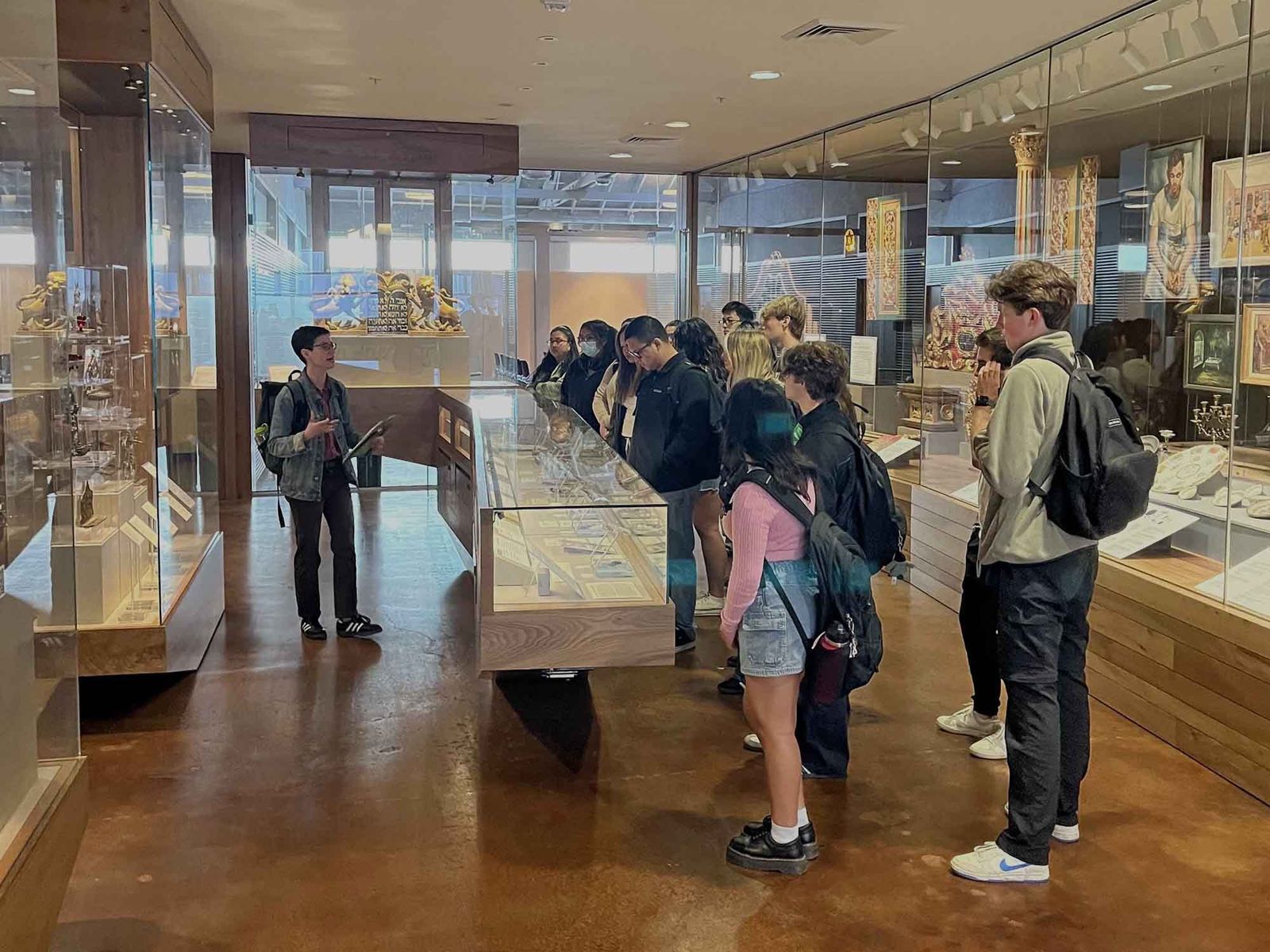 Visitors looking at objects in glass cases in a gallery with wooden floors.