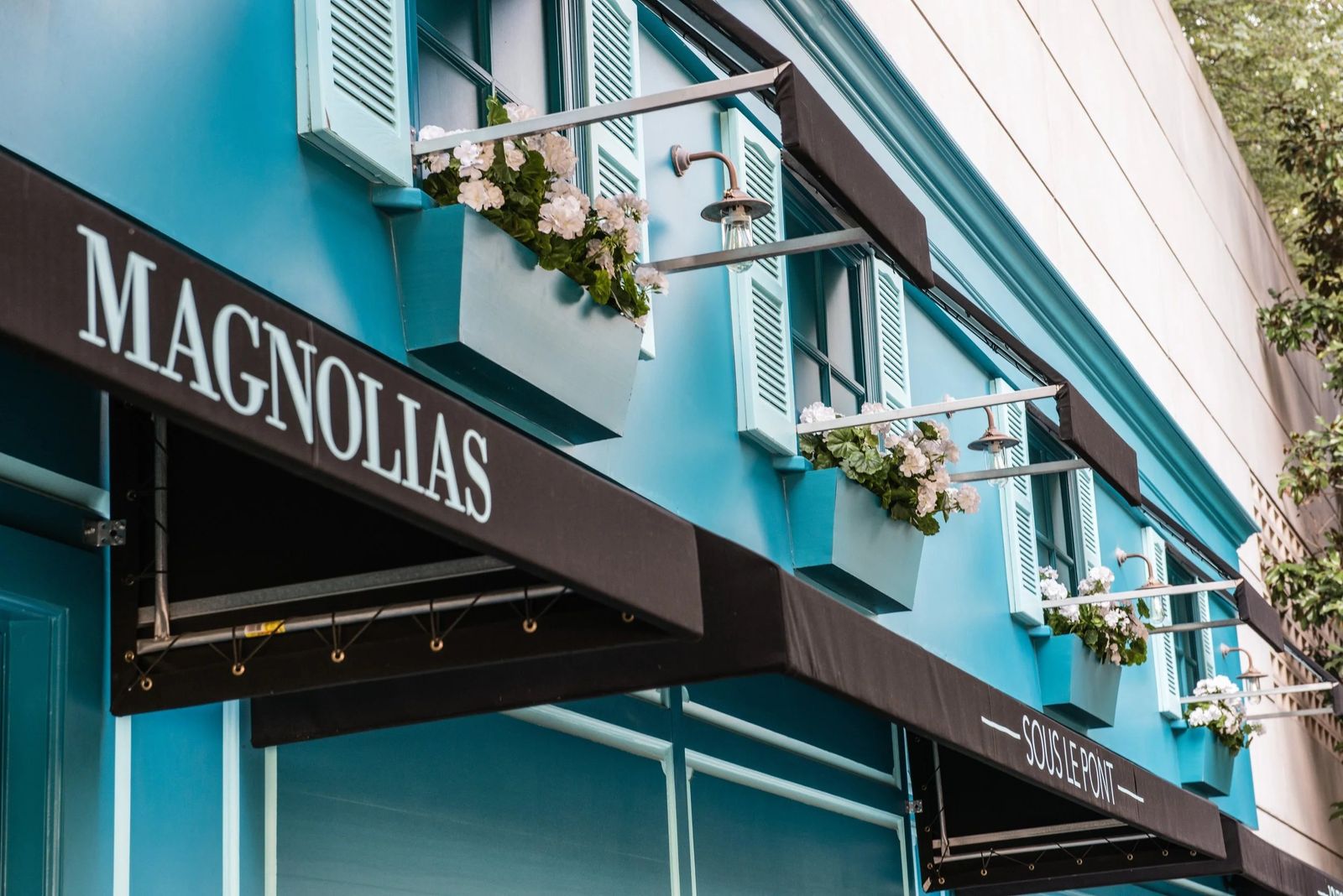 A teal storefront with a dark awning that reads Magnolias and flower boxes in the upper windows.