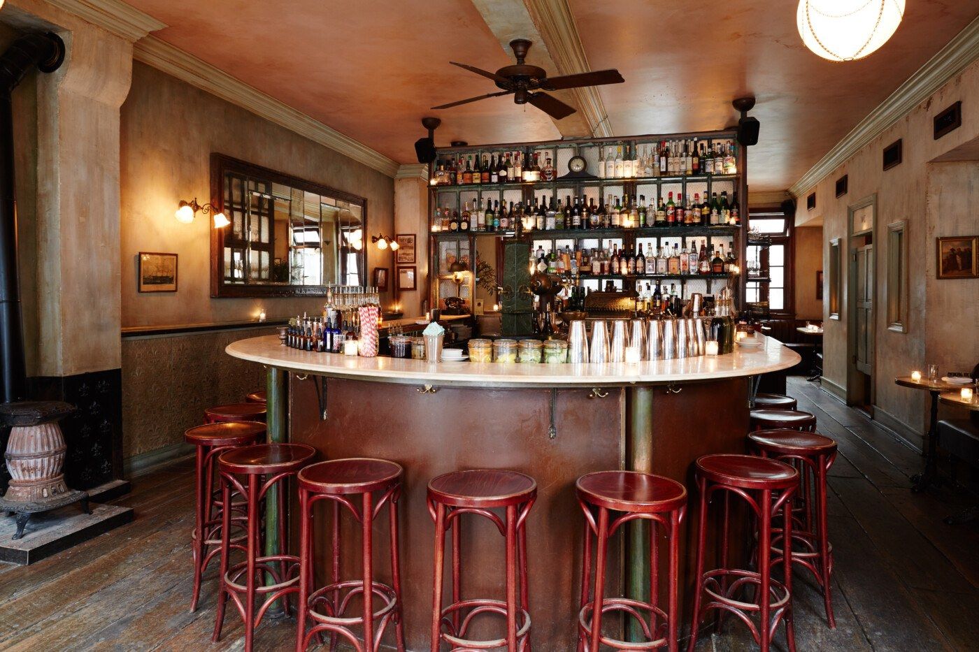 A round bar with red stools and shelves of bottles in a vintage-style room