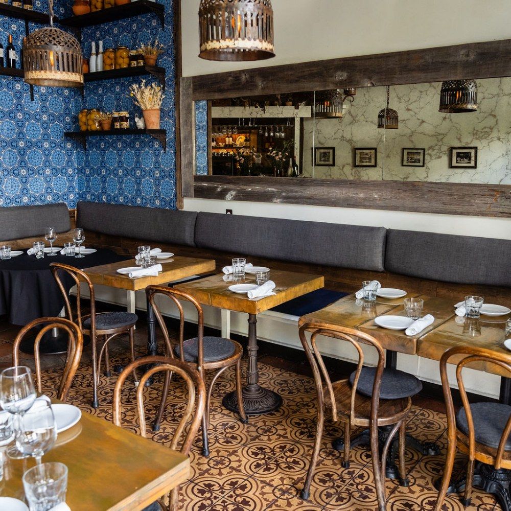 Dining room with gray banquettes, wooden tables, bentwood chairs and blue tile behind the bar