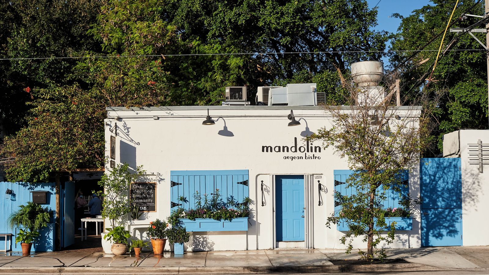 White building with blue shutters and doors surrounded by trees and plants