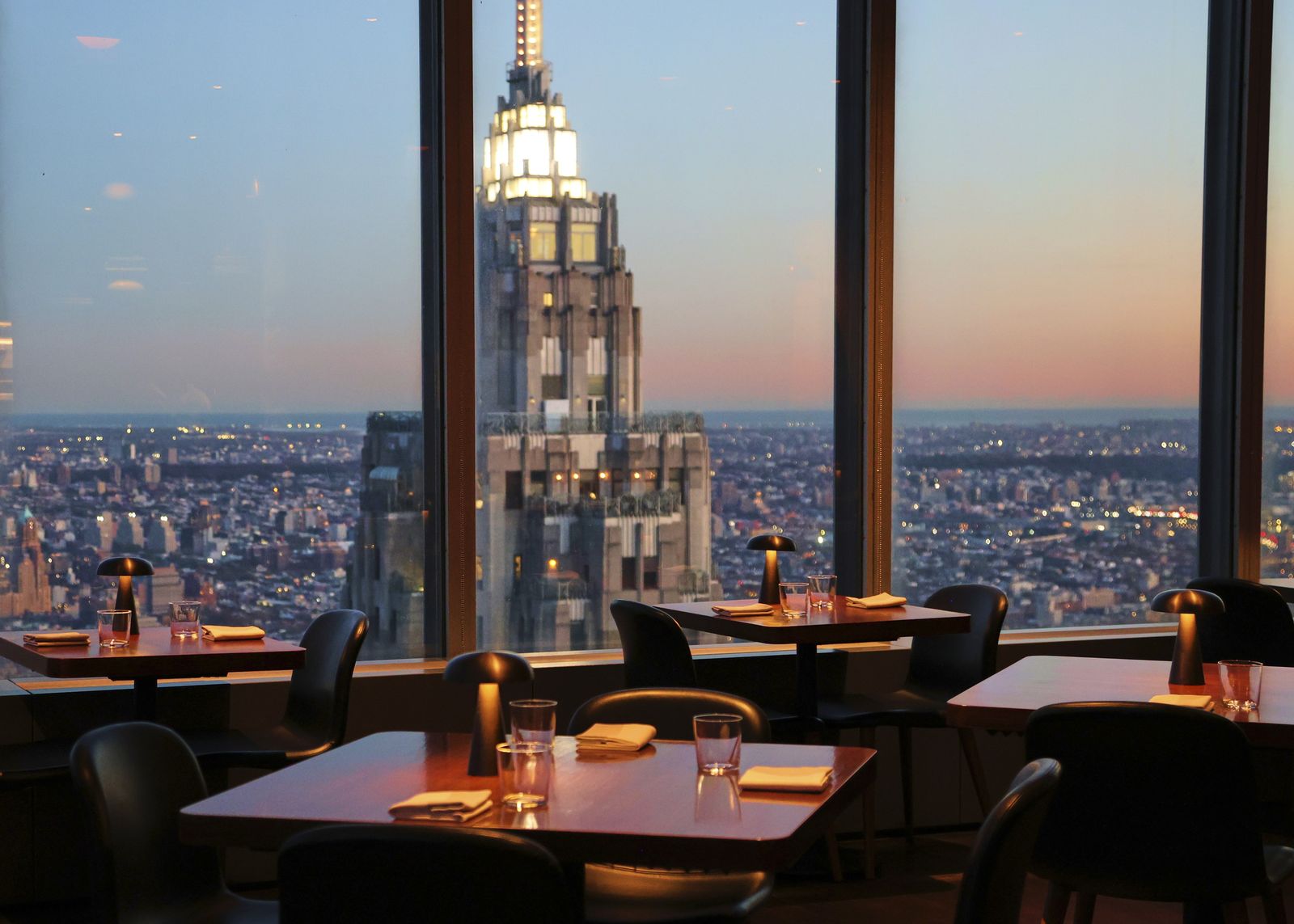 Dining room tables at dusk with large windows framing the Empire State Building and city lights