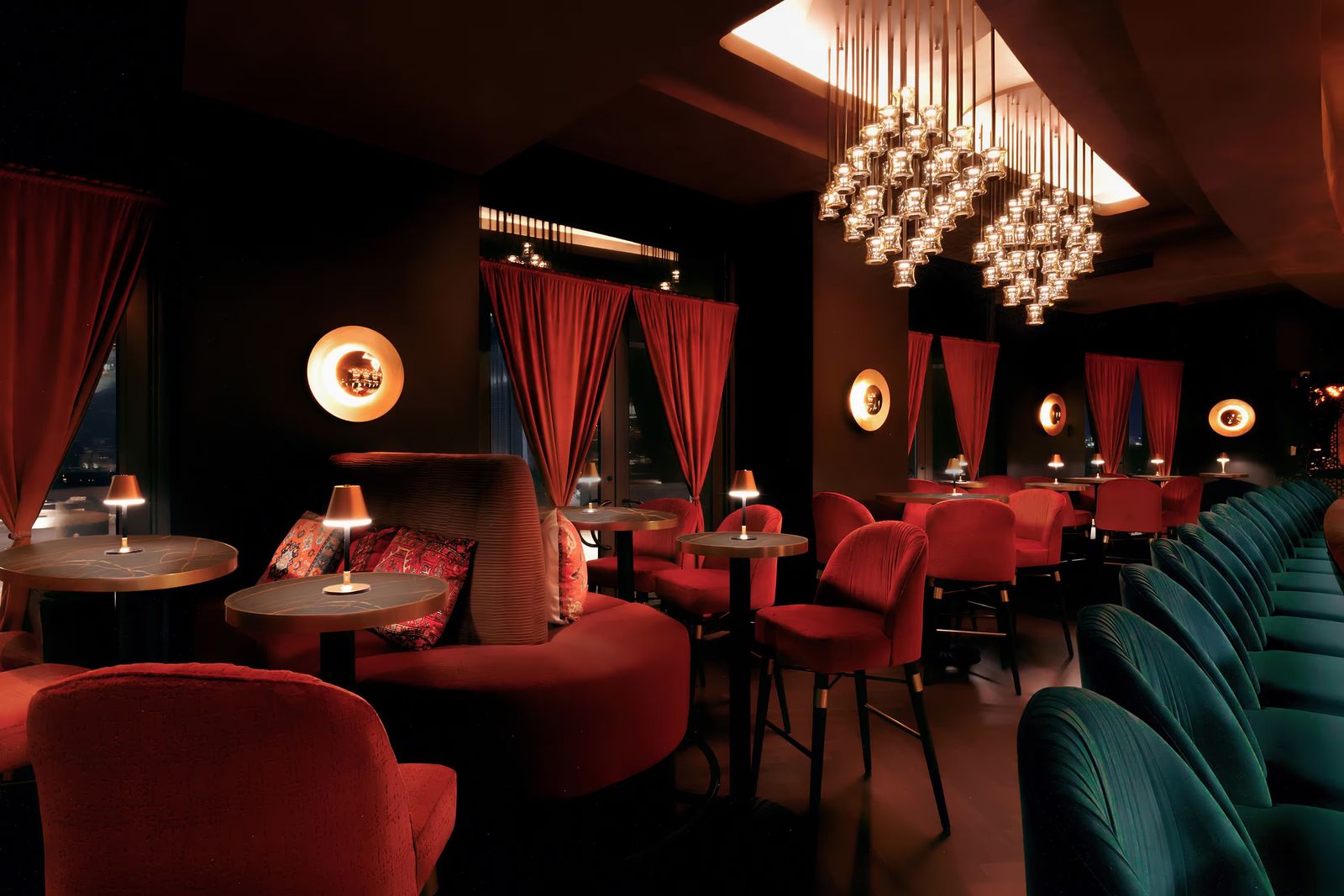 Dimly lit bar and lounge with red and teal seating, curtains and a chandelier