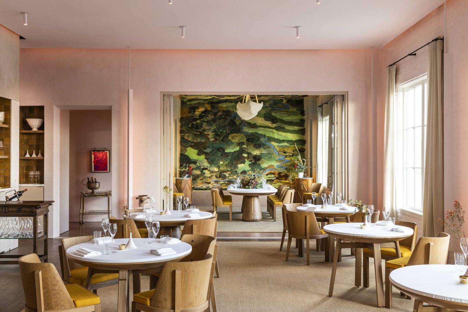 Pink-walled dining room with round tables, chairs and a large mural on the far wall