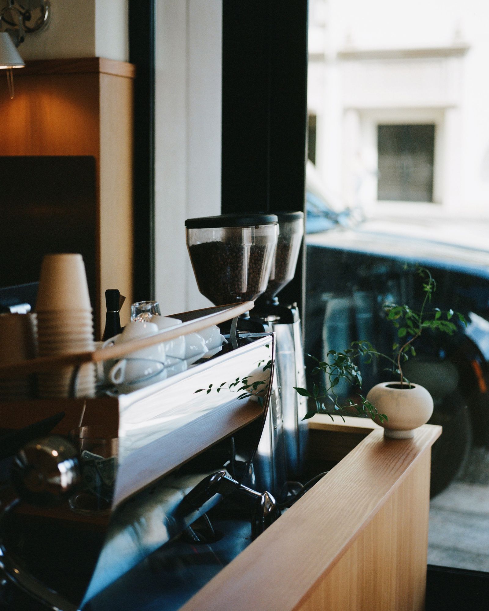 An espresso machine and grinder on a light wood counter beside a window.
