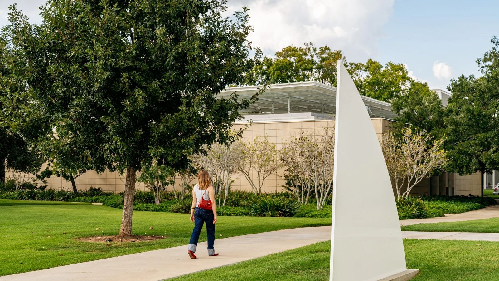 A visitor walking along a path on the lawn past a white sculpture with the museum building behind