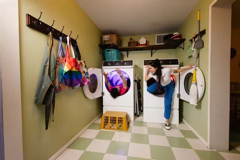 A room set like a laundry nook with washers and dryers, hanging clothes and a checkered floor.