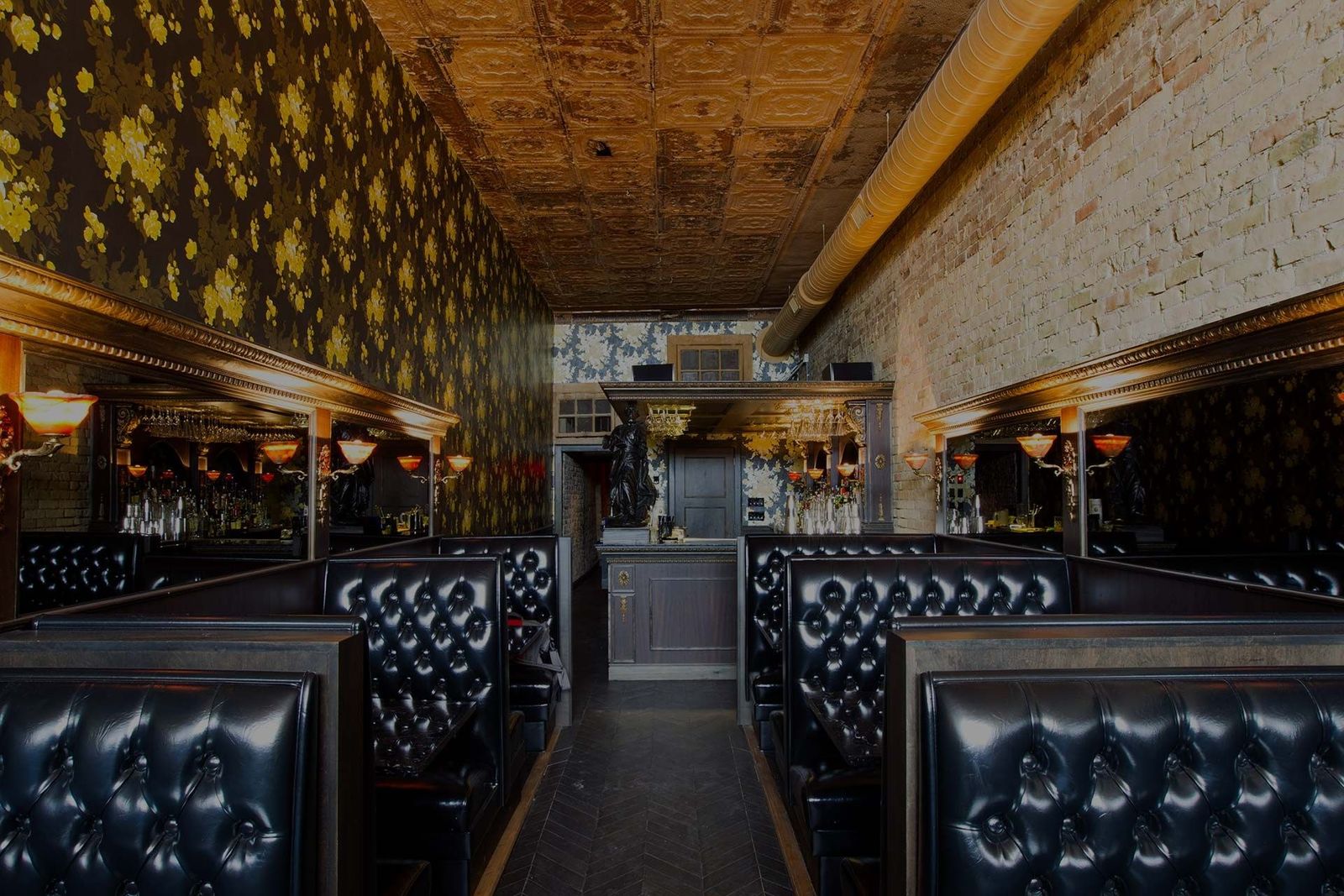 A narrow bar room with black tufted leather booths along both walls under a gold patterned ceiling.