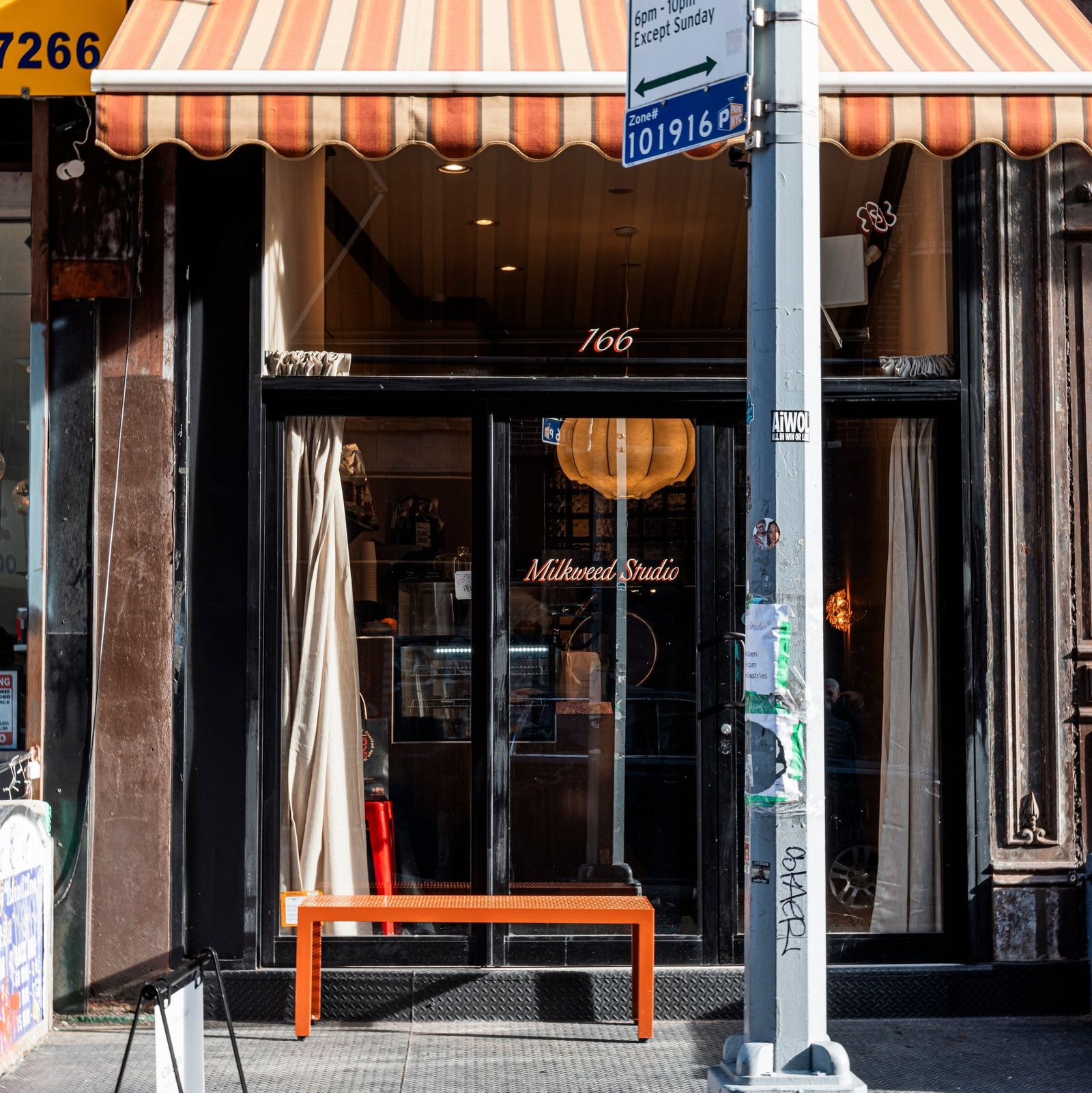 A storefront with a striped orange awning, dark windows with the shop name on the glass and an orange bench out front.