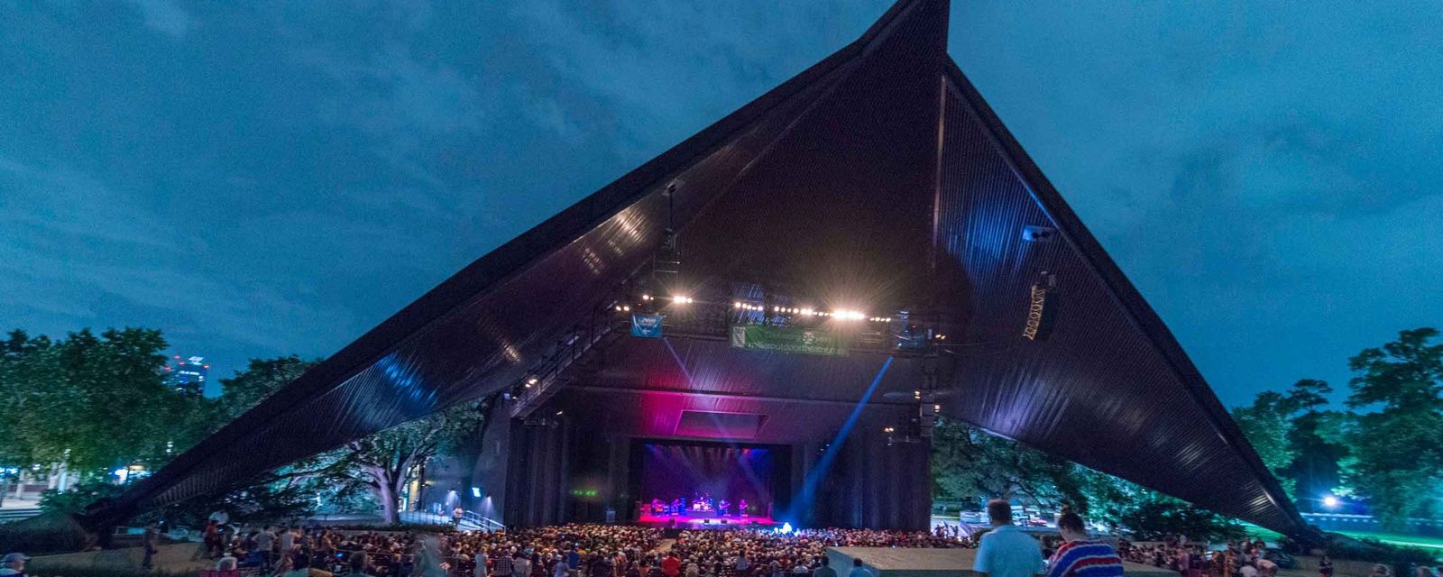 Miller Outdoor Theatre's angular covered stage at dusk with a crowd on the lawn