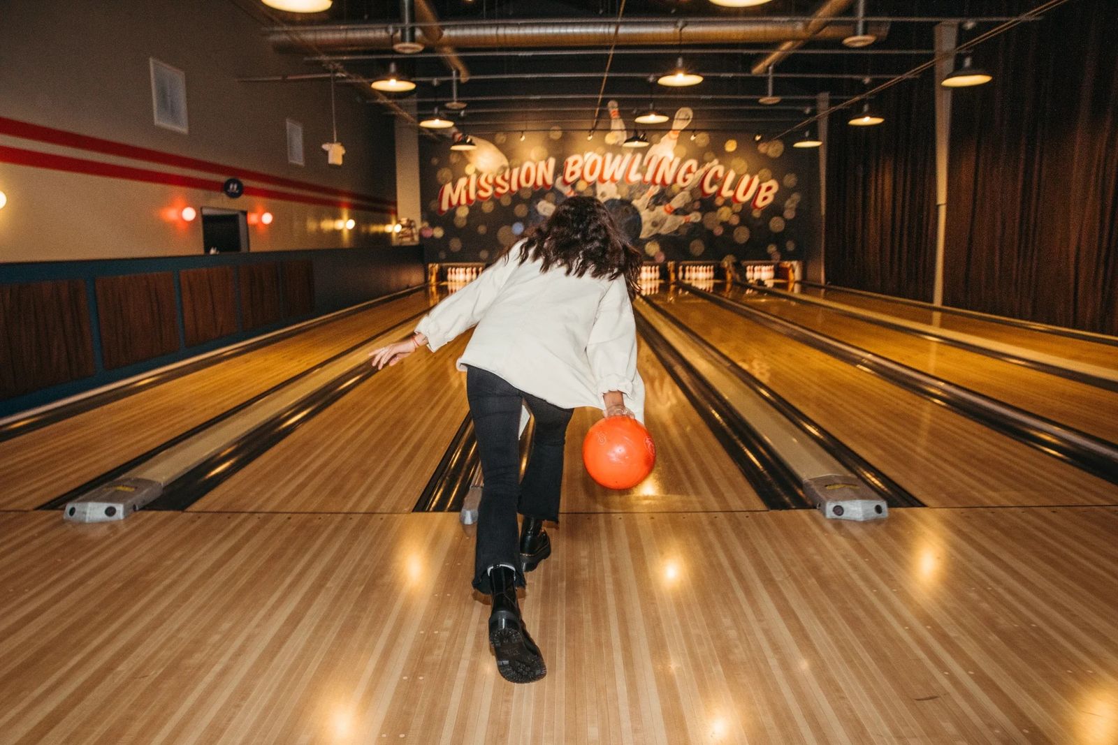 A bowler mid-throw on a lit lane under a sign reading Mission Bowling Club.