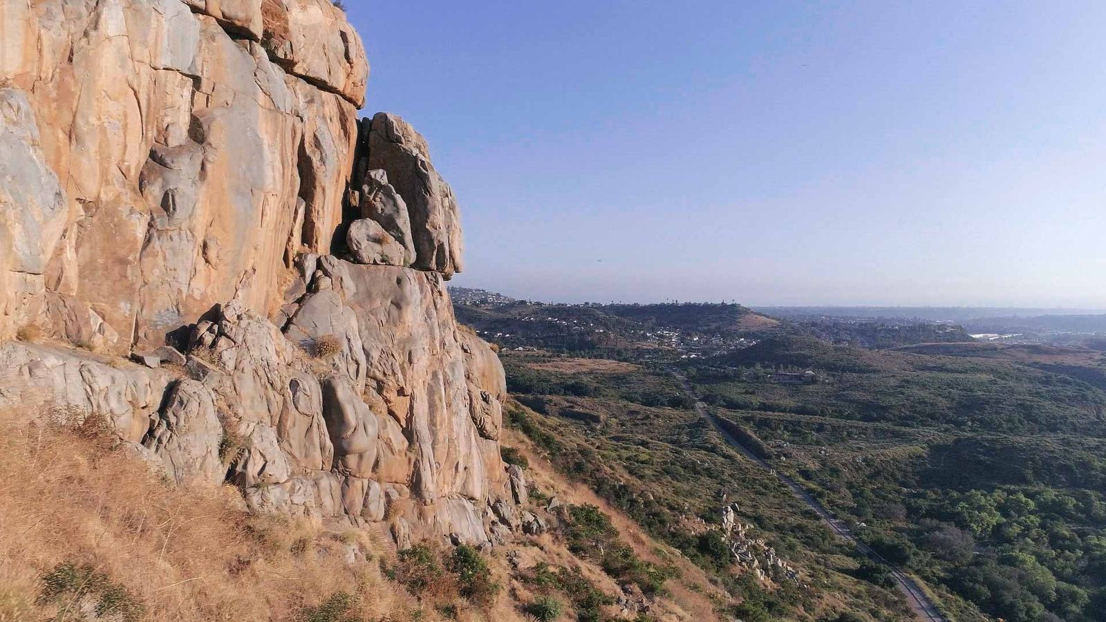 A rocky cliff face above a wide valley under a clear sky.