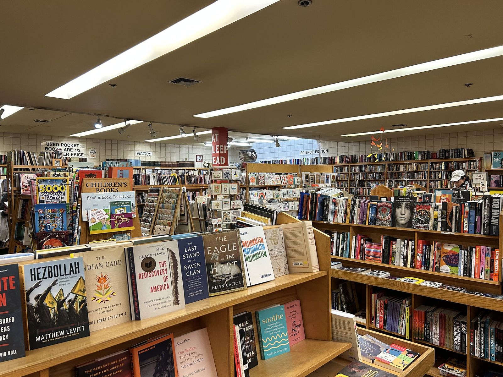 Aisles of a large used bookstore with shelves, stacked tables and paperbacks displayed in front.