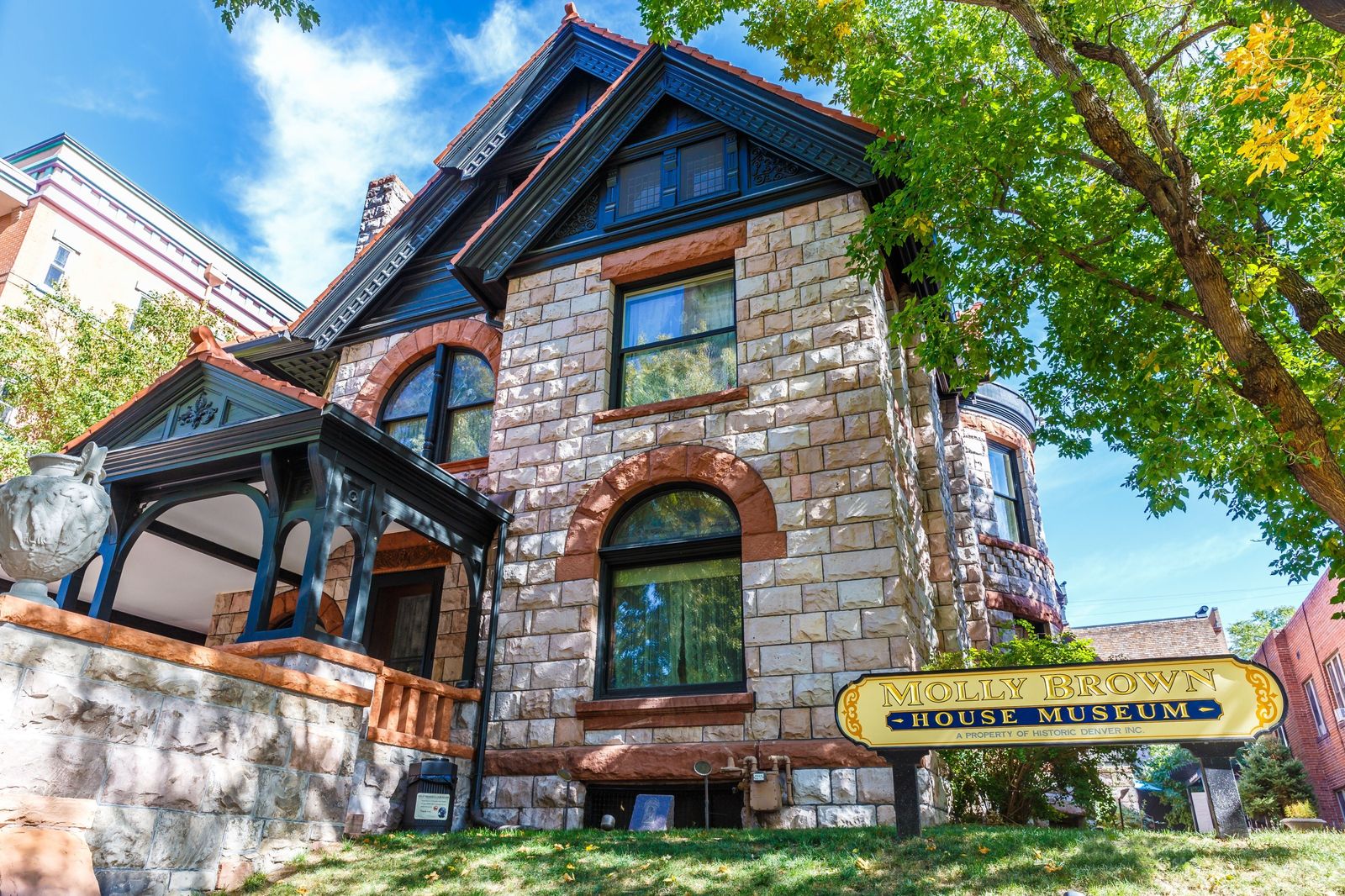 The stone mansion's gabled front with arched windows and a museum sign, under a blue sky.