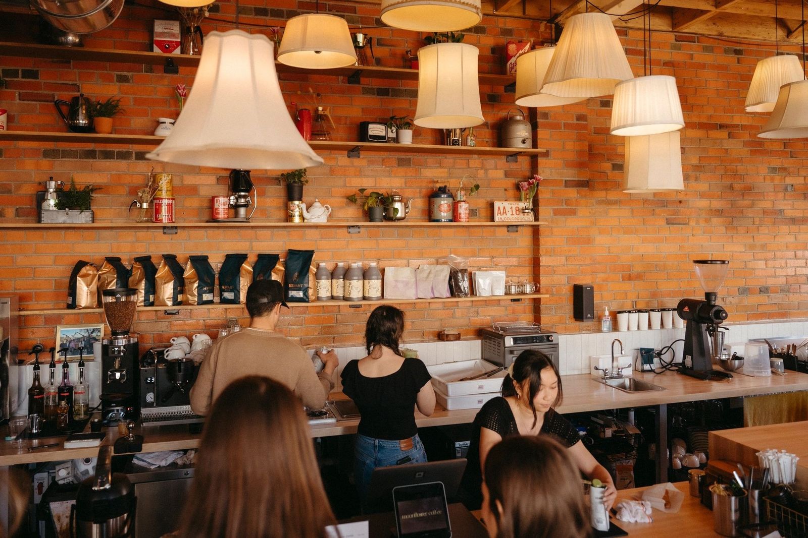 A brick-walled cafe with pendant lamps over a counter lined with shelves and baristas at work.