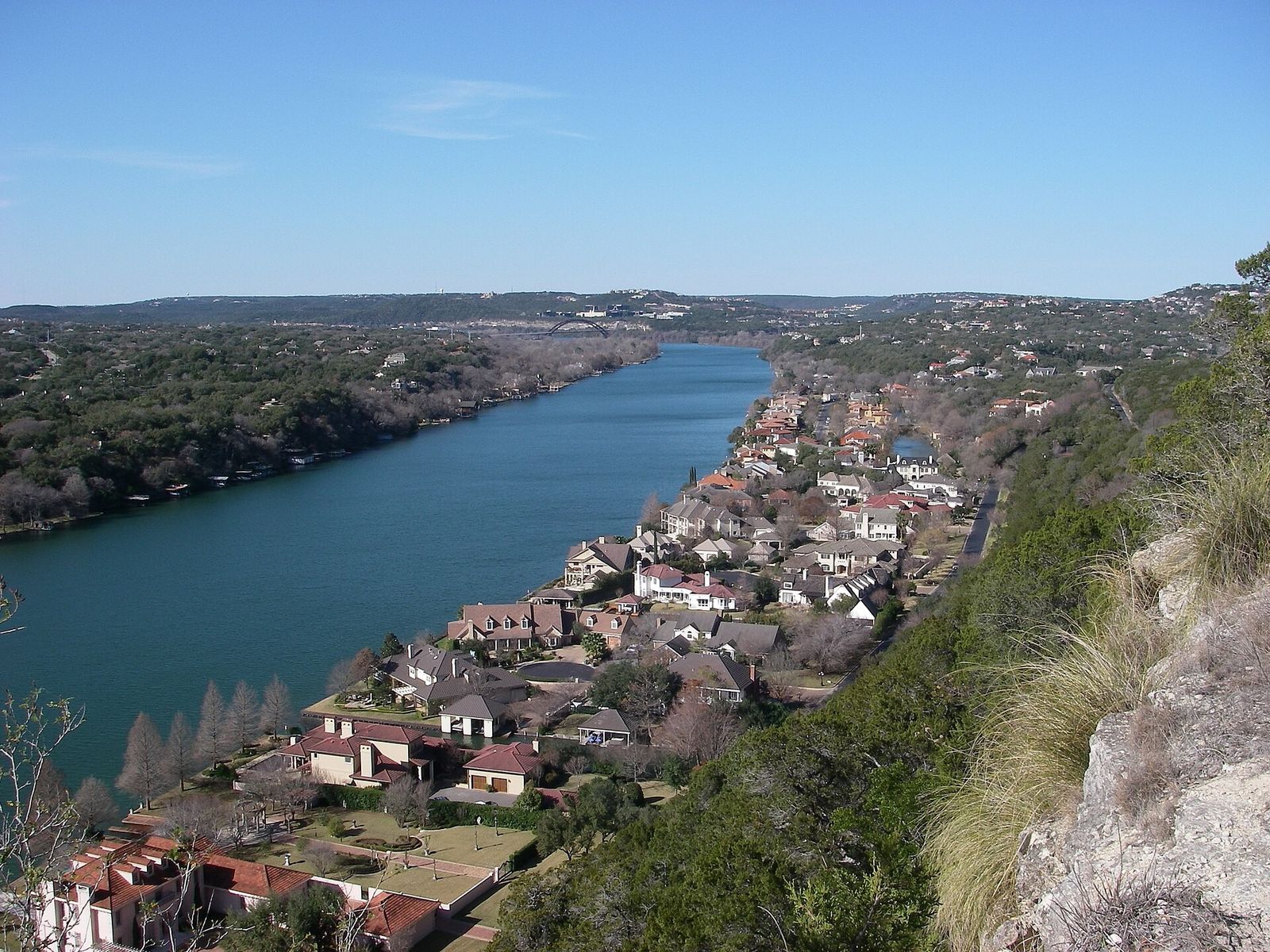 A river bending below a limestone cliff, with houses along the hillside on the opposite shore.