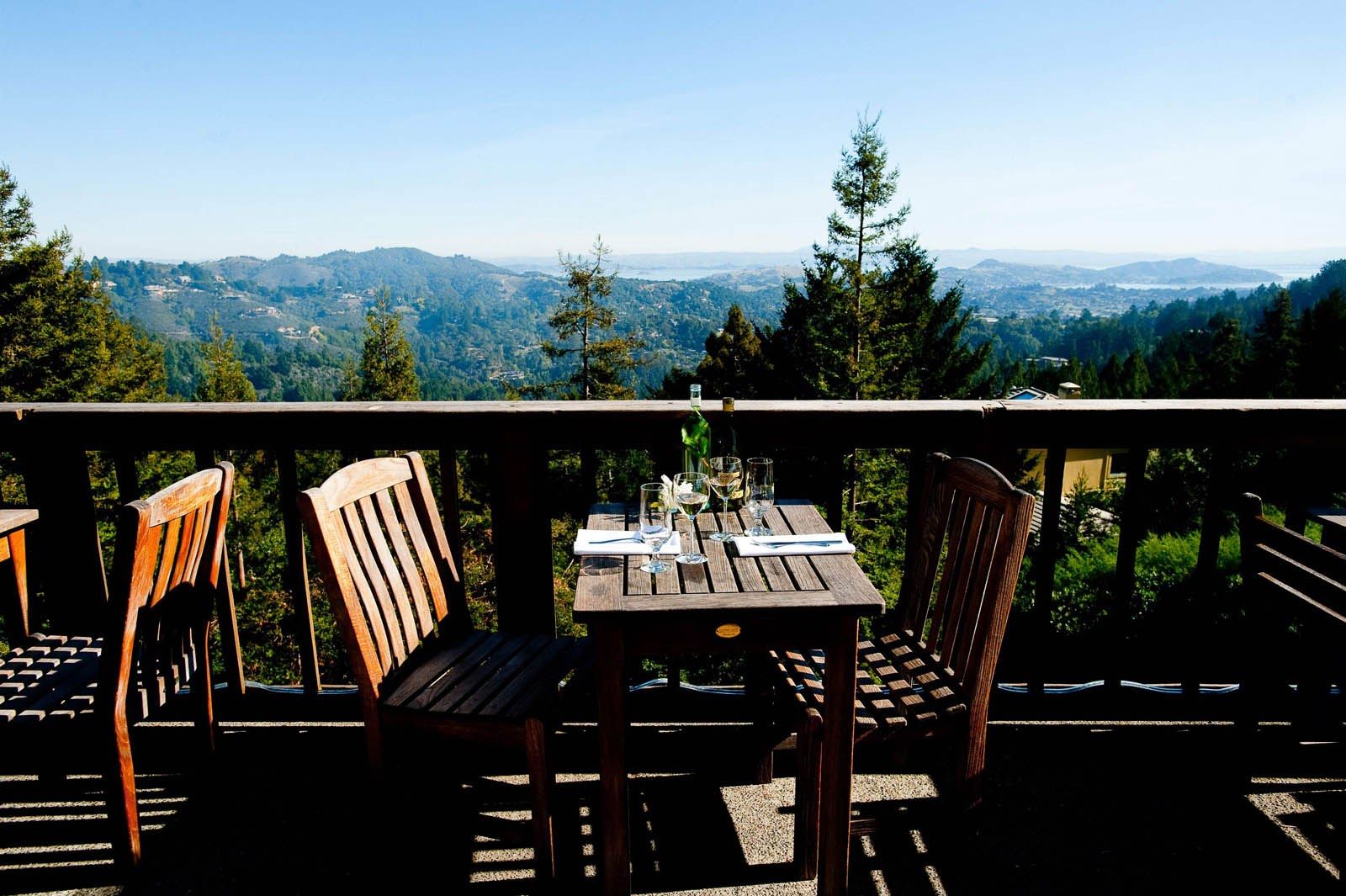 Wooden deck tables and chairs overlooking forested hills and distant bay