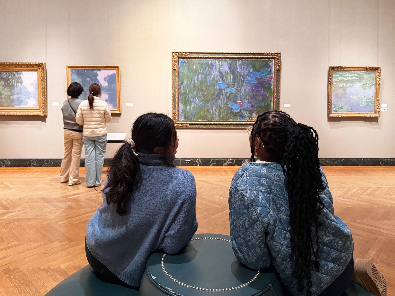 Two visitors seated on a bench in a gallery facing a framed water lily painting