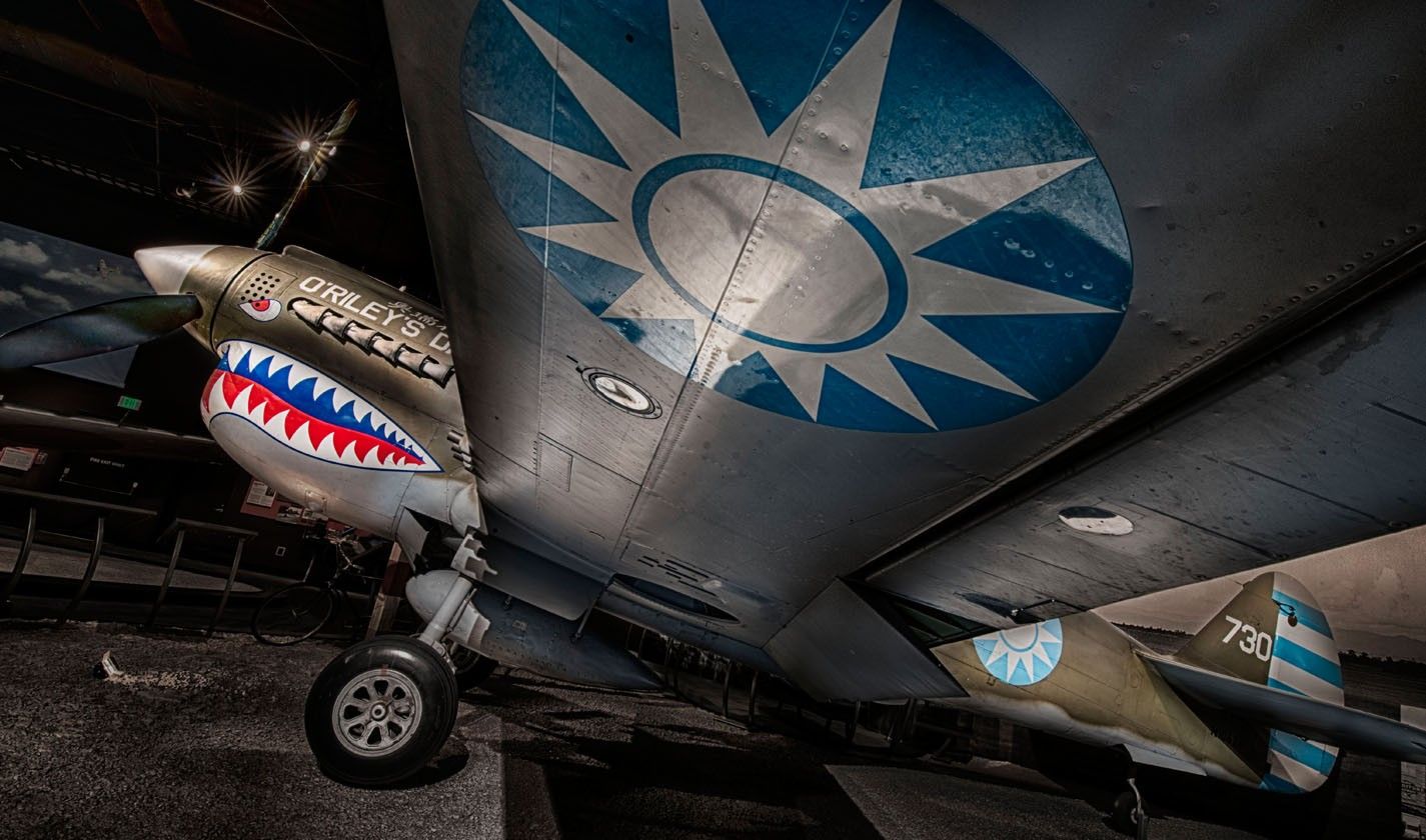 A vintage fighter plane with a shark-mouth nose painted on it, seen up close in a museum hangar.