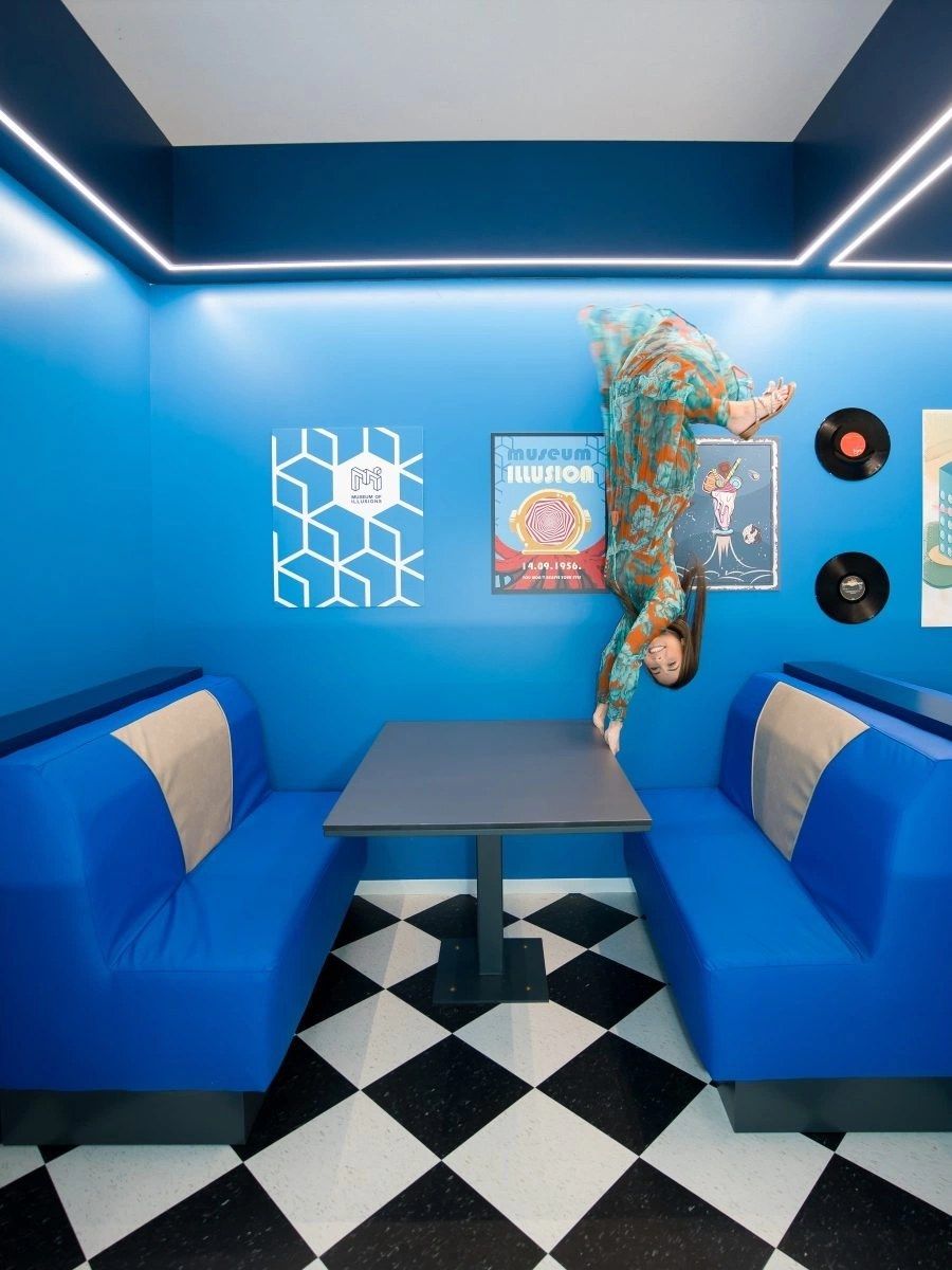 A blue booth with checkered flooring and a woman appearing to lie sideways on the ceiling.