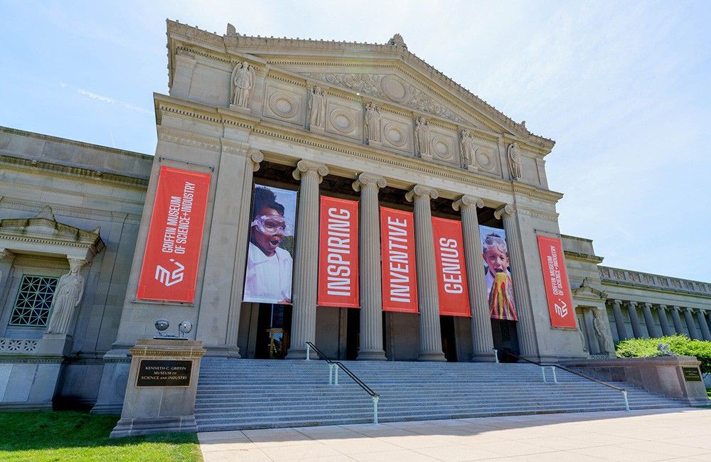 The columned stone front of the museum with red banners hung between the columns, above wide steps.