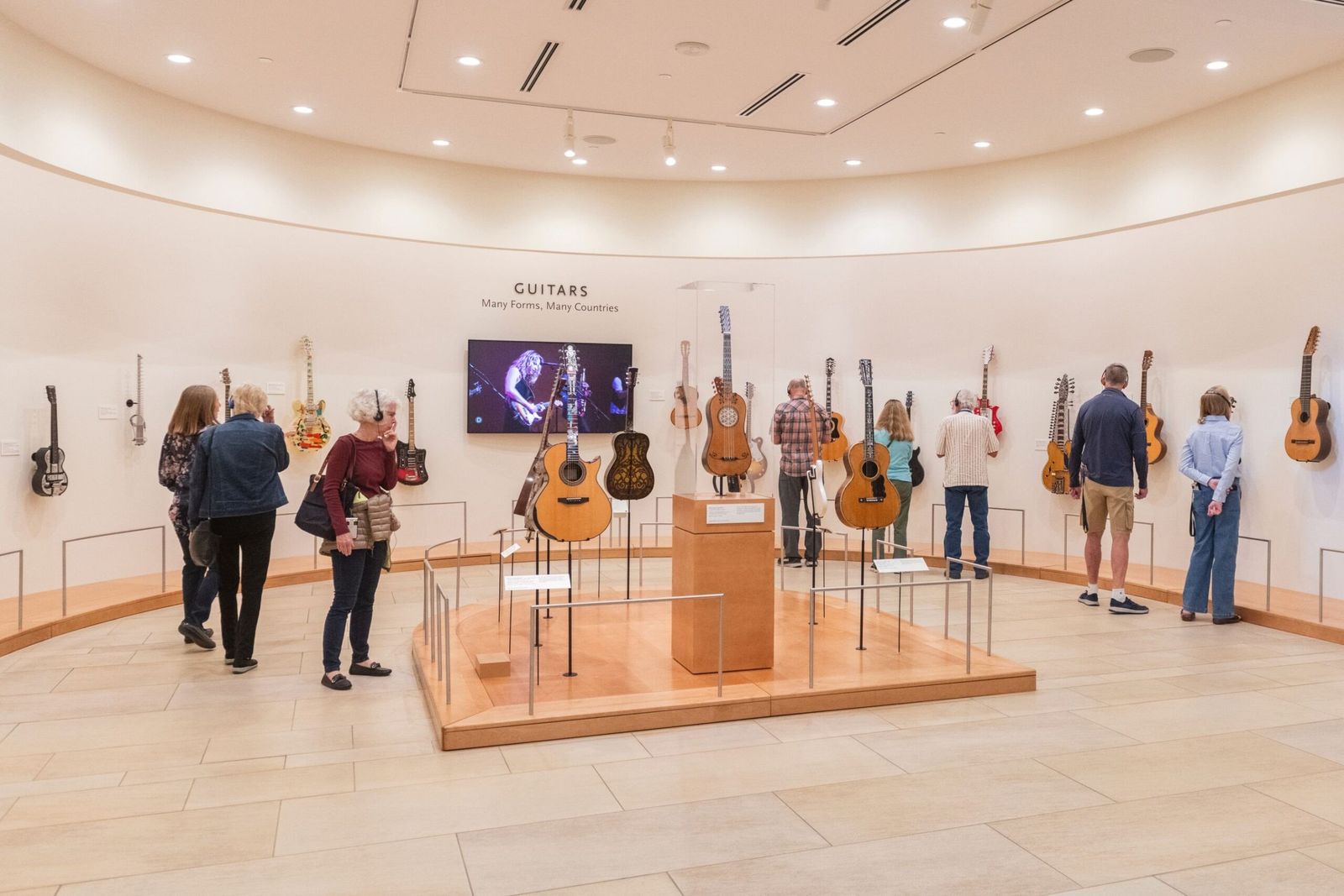 A bright museum gallery with guitars displayed on a round platform and a few visitors