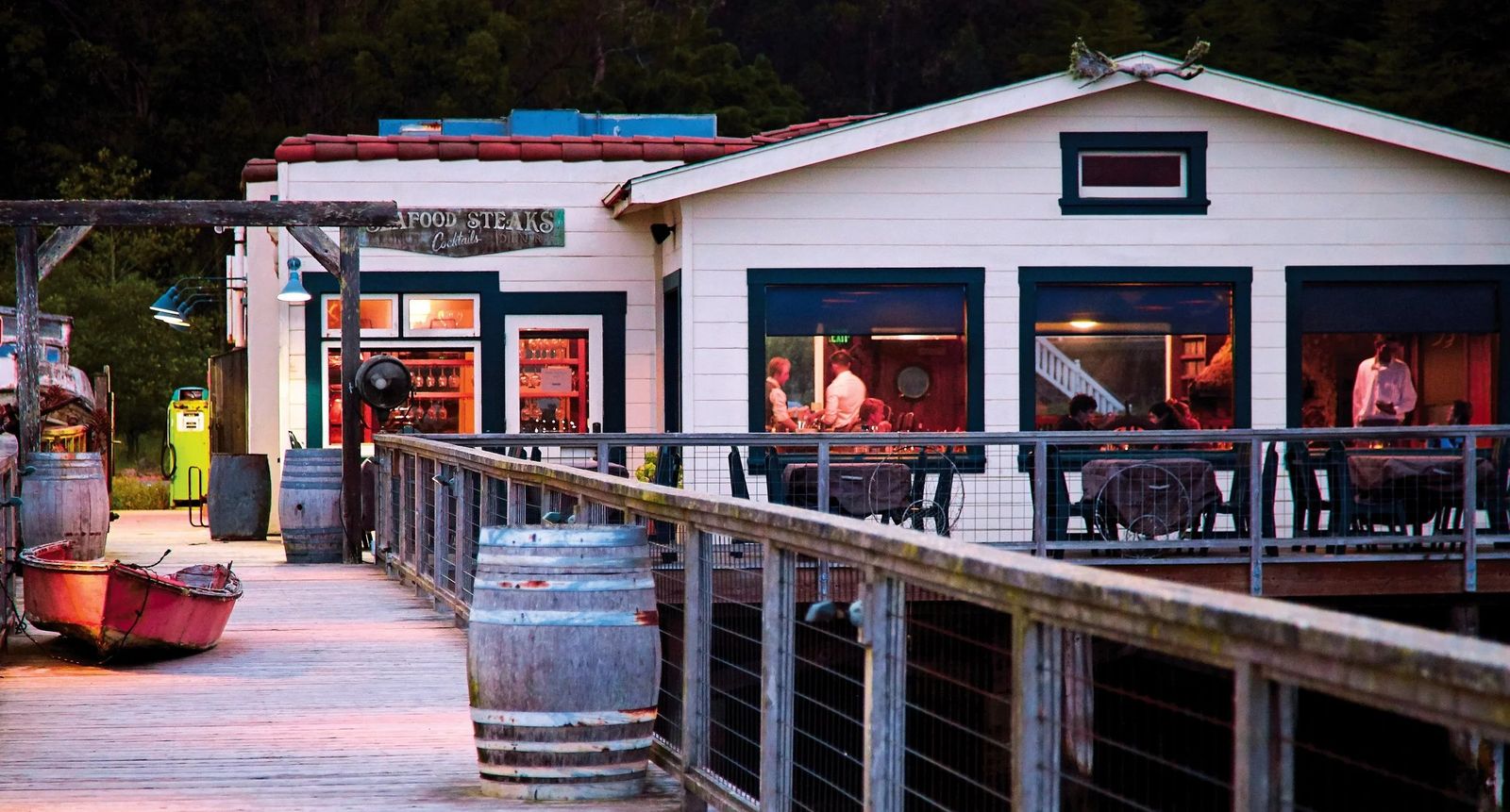 White waterfront restaurant building with a deck, railing and wine barrel