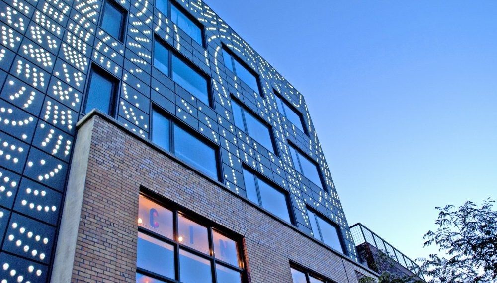 Exterior of a modern brick and glass building with a pattern of white dots on dark panels against blue sky