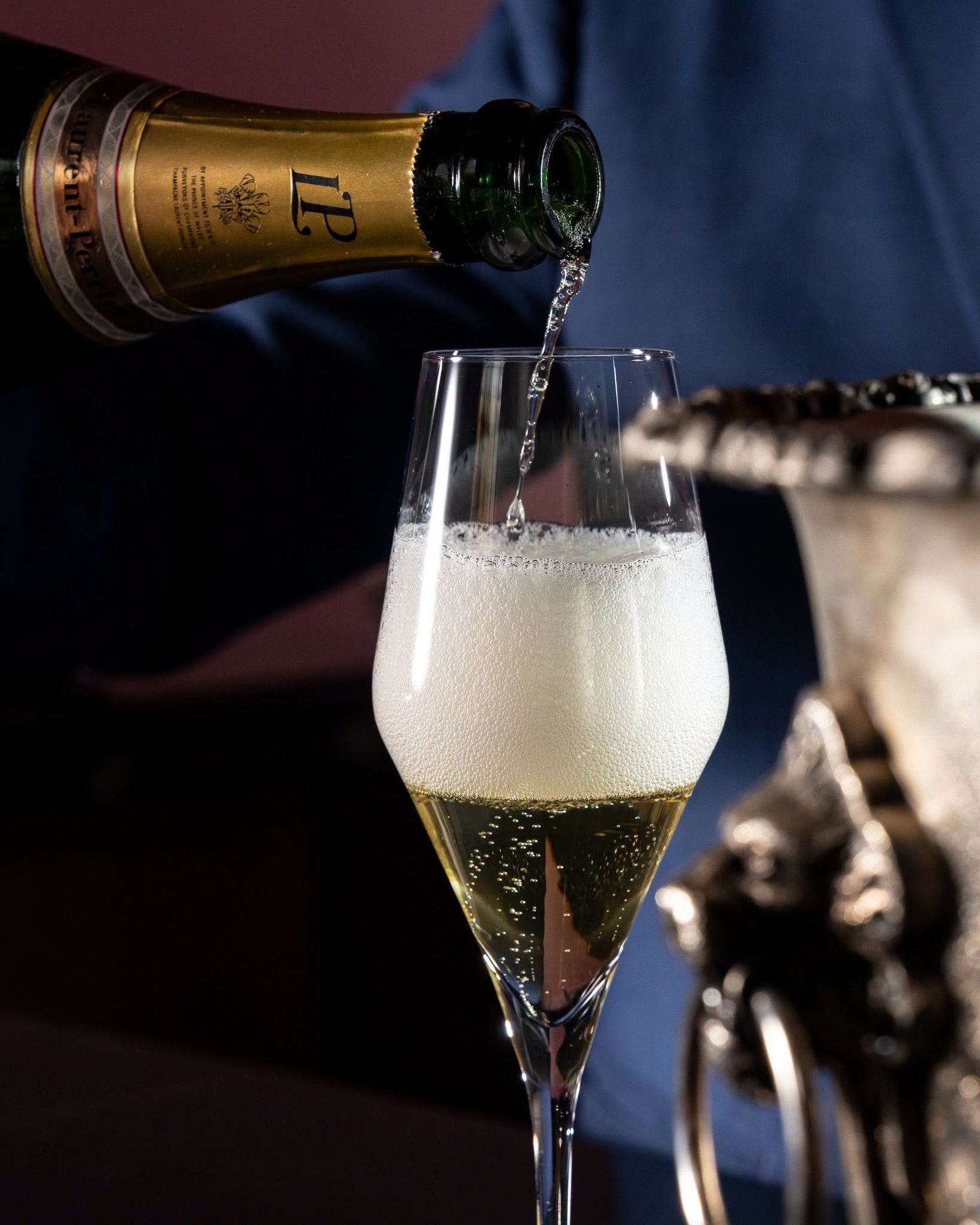 Champagne being poured into a flute, with the bottle's neck and a metal ice bucket in view.