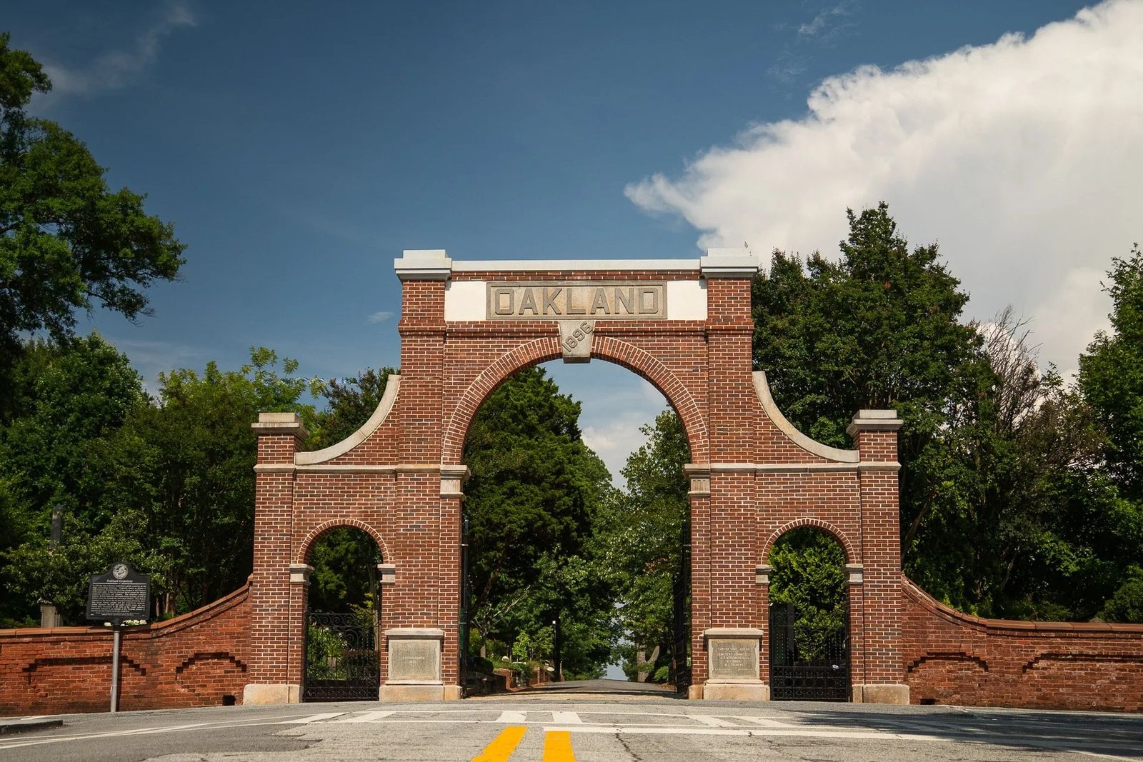 A red brick archway gate reading Oakland over a road, framed by trees and sky
