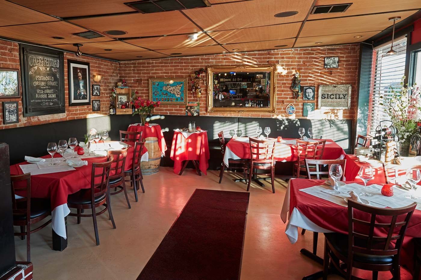 A restaurant room with red-clothed tables and wooden chairs, brick walls and framed photographs.