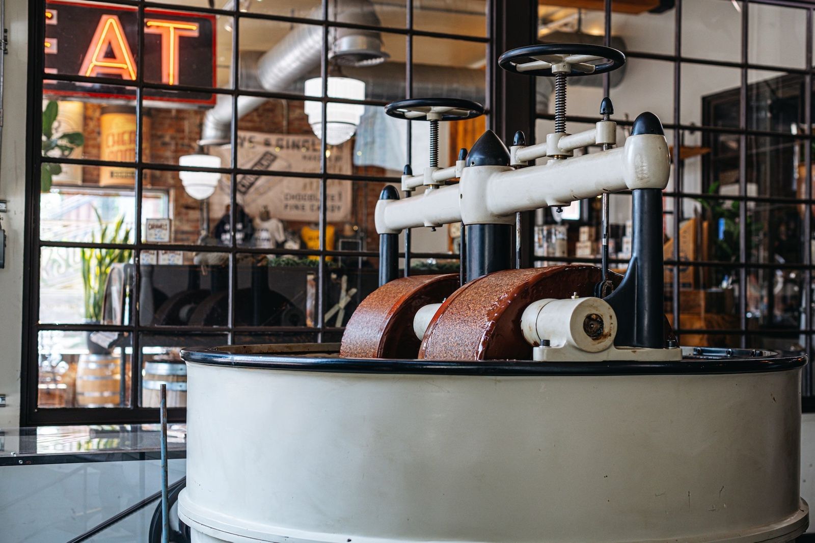 Chocolate stone grinder machine inside the factory with a window and sign behind it