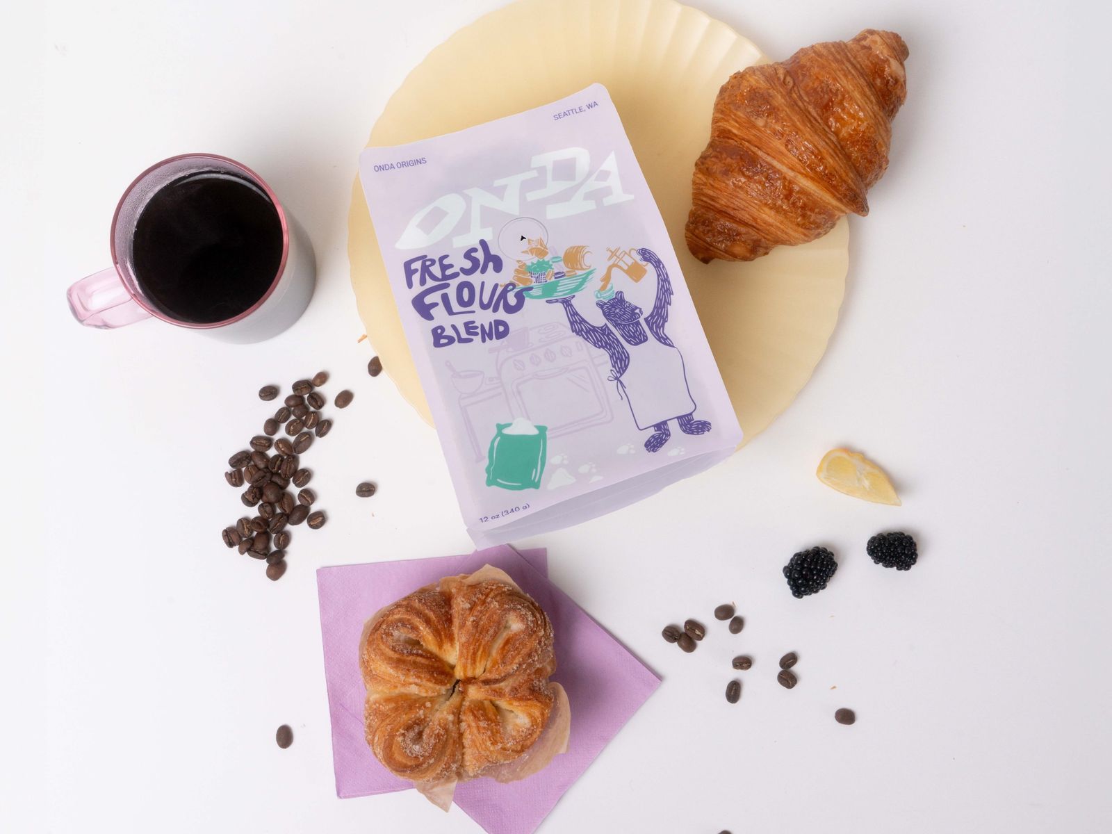 A cup of black coffee, a bag of coffee beans and two croissants on a plate, seen from above.