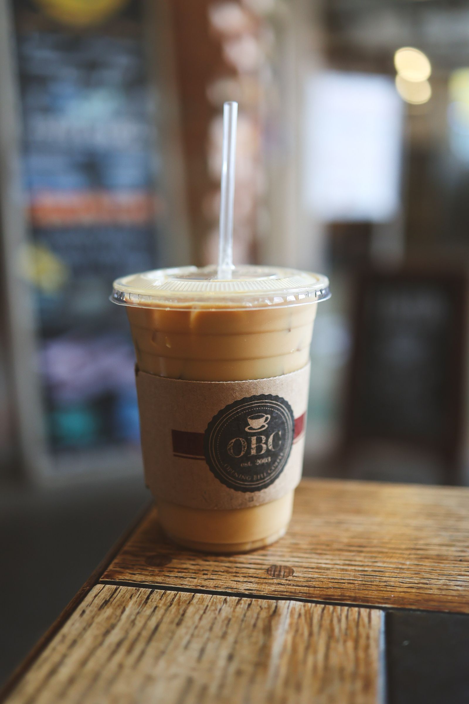 An iced coffee in a clear plastic cup with a branded sleeve on a wooden table.