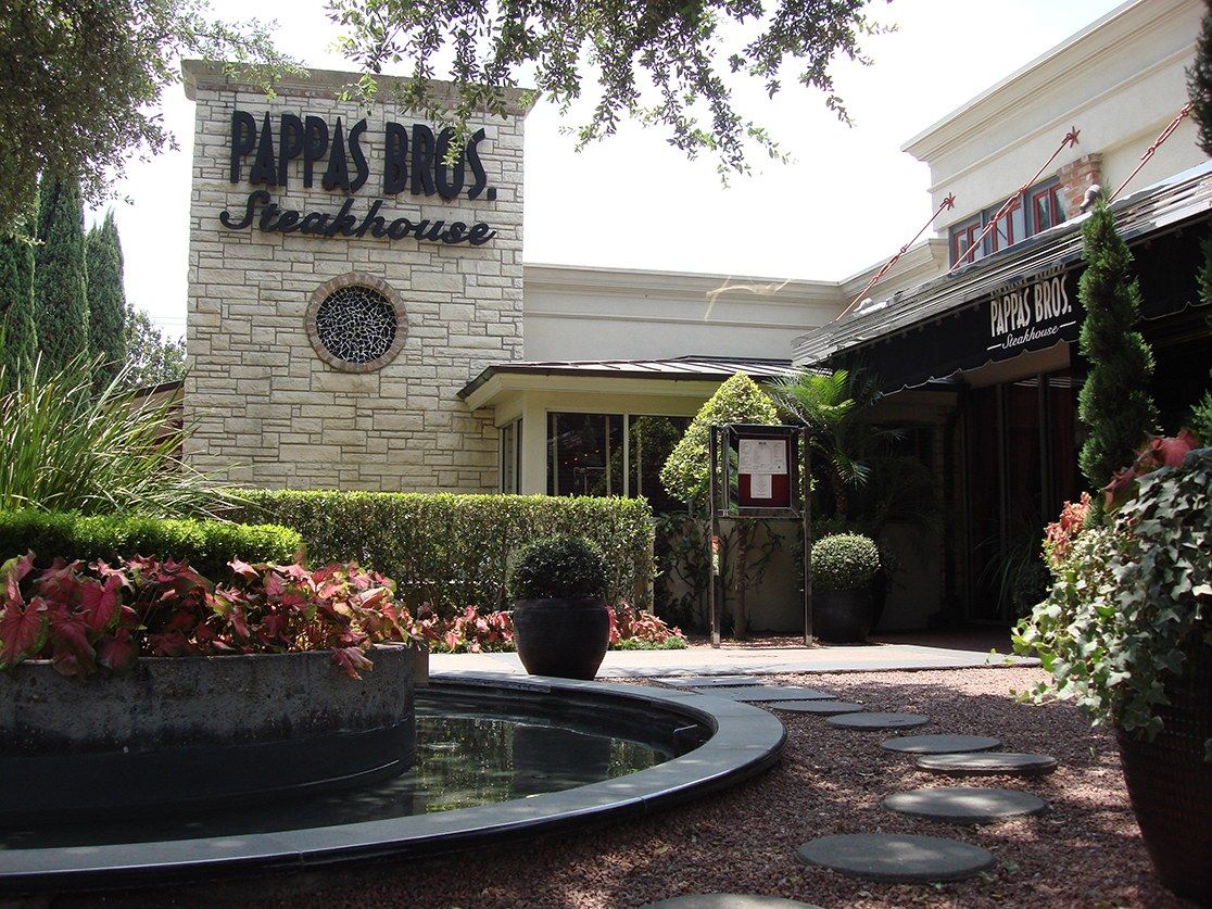 Stone entrance of the steakhouse with its sign, a fountain pool and landscaped plants