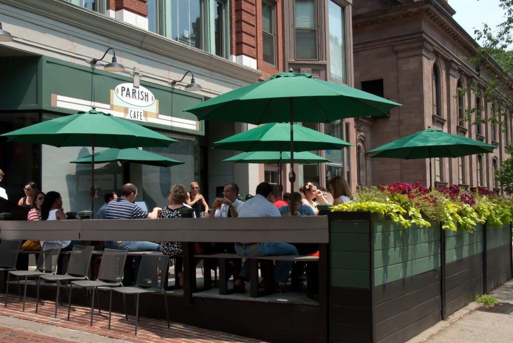 Parish Cafe patio with green umbrellas, outdoor tables and diners in front of a brick building