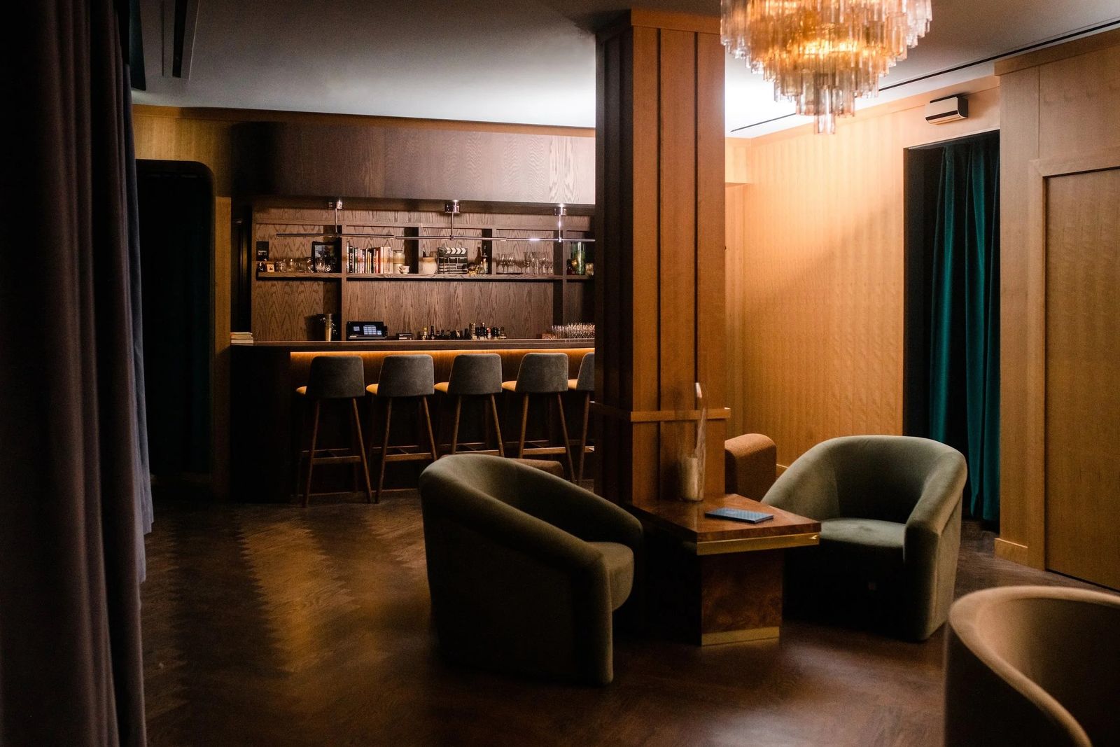 Dim lounge with armchairs and a wood-paneled bar with stools