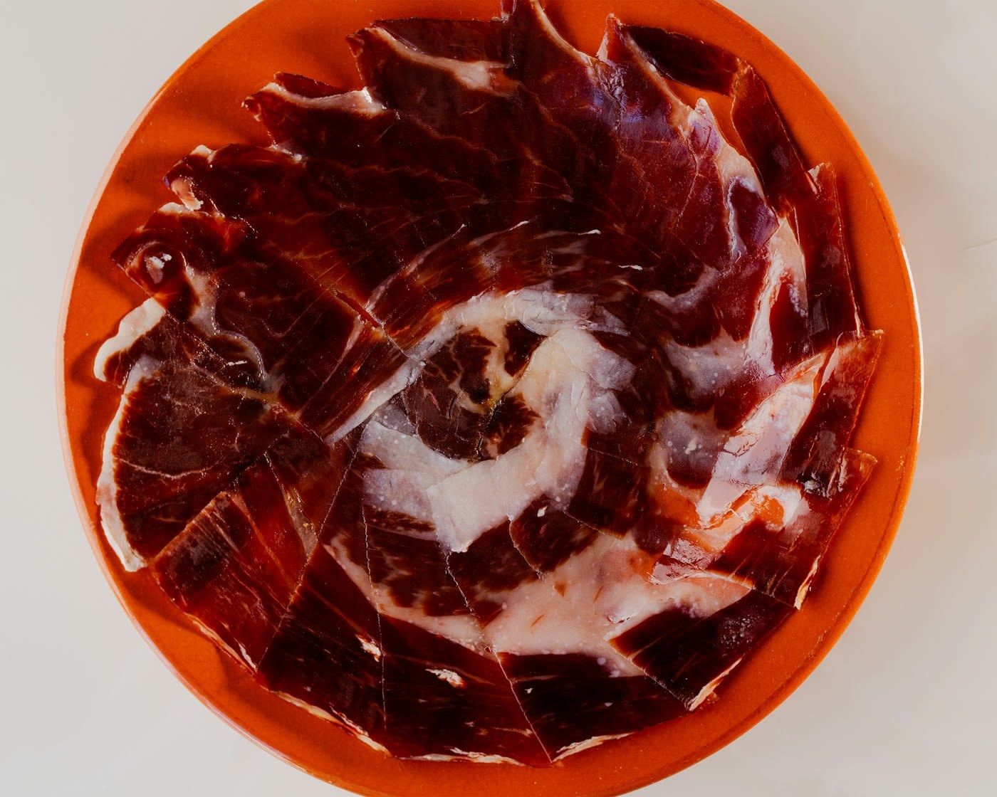 Plate of thinly sliced cured ham fanned on an orange plate