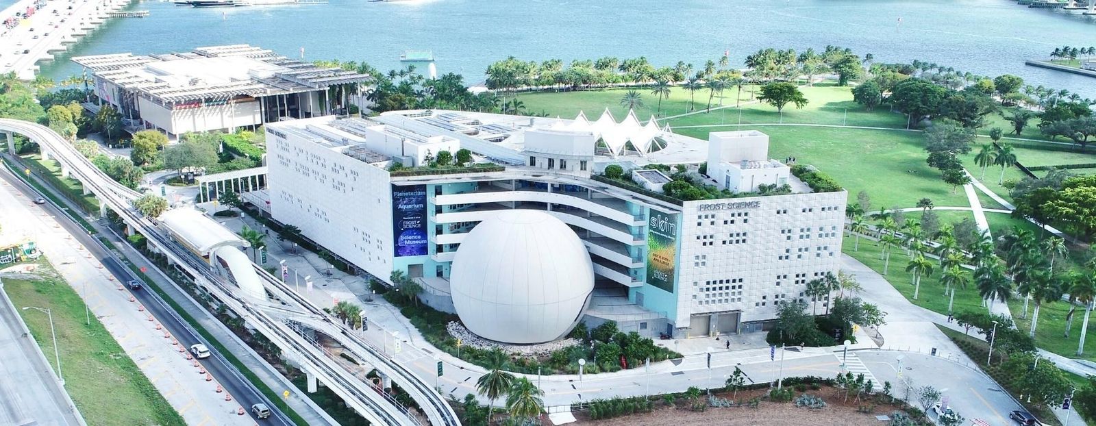 Aerial view of the Phillip and Patricia Frost Museum of Science building and its round planetarium dome beside the water
