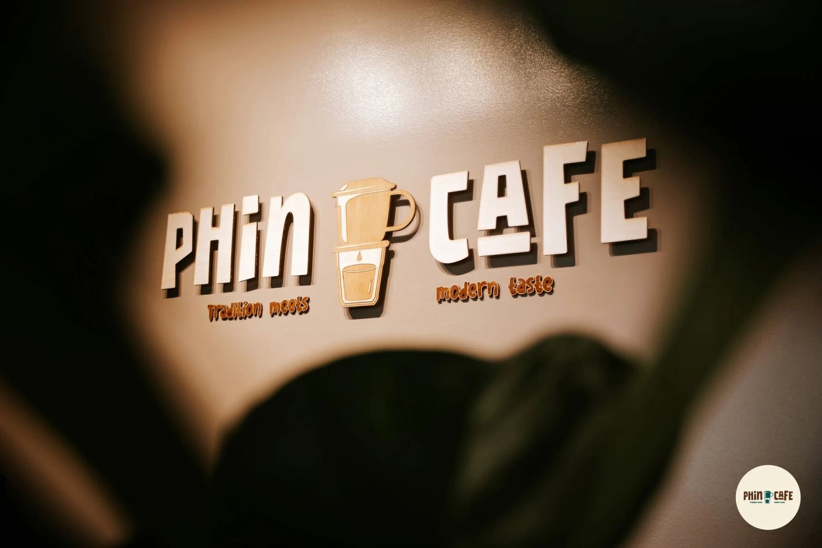 A wall sign reading Phin Cafe with a drip coffee filter icon and the line Tradition meets modern taste.