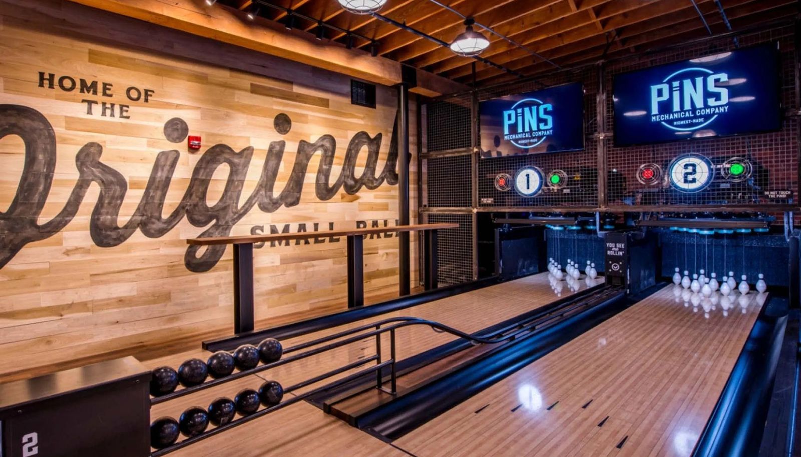 A bowling lane with a wood-paneled wall reading Home of the Original, with scoreboards above the pins.