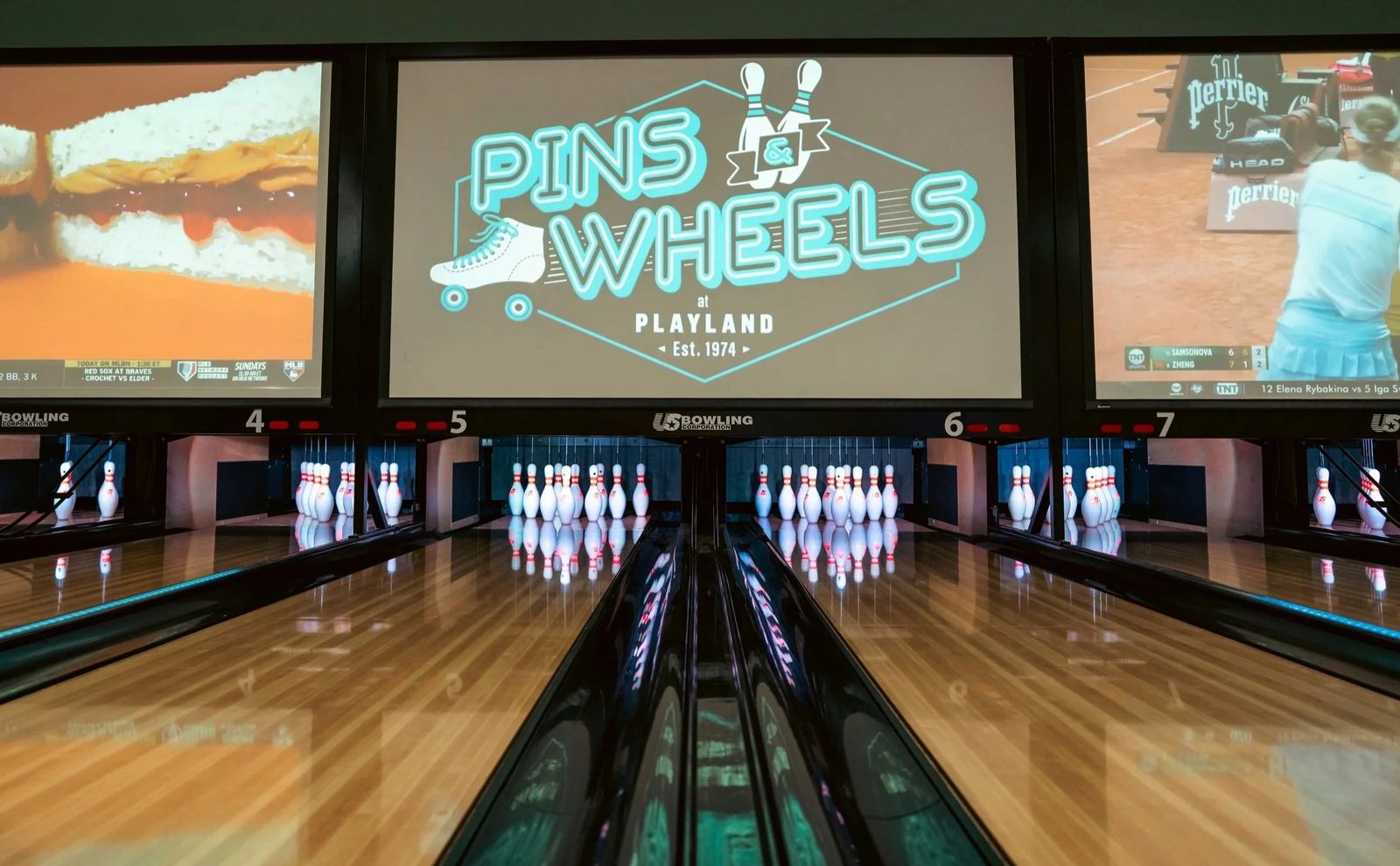 Rows of bowling lanes with a large screen above the pins in a dim room.
